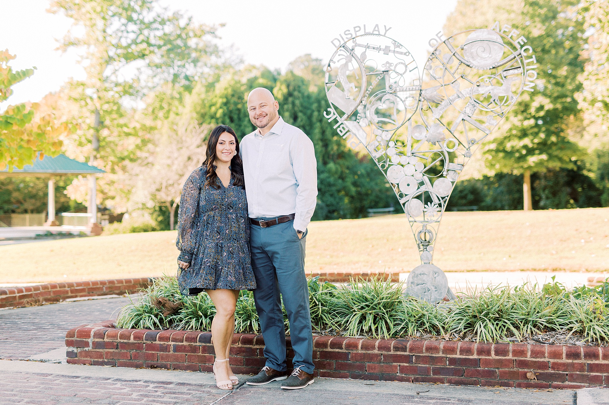 couple poses by statue in gardens of Downtown Matthews