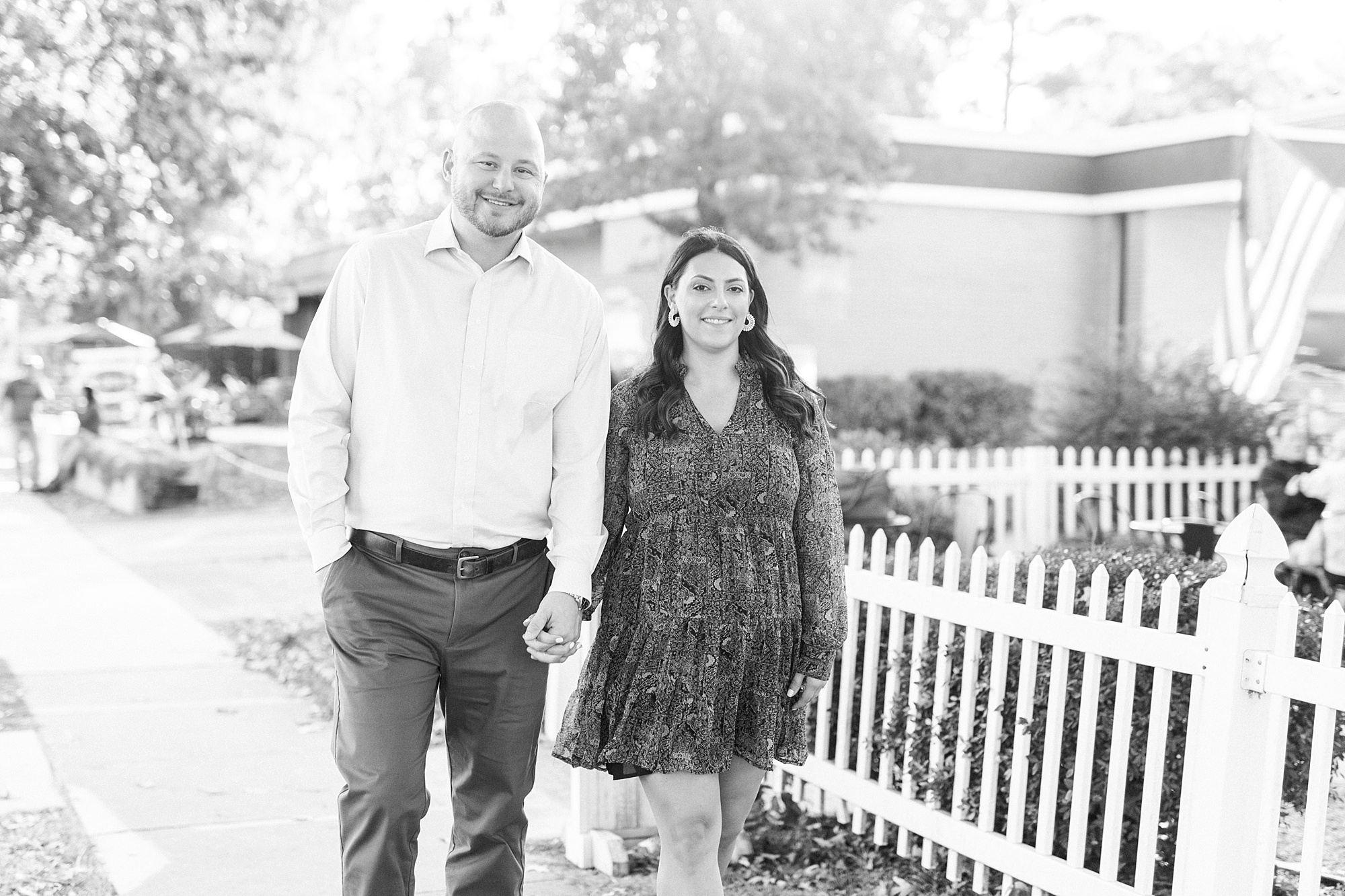 bride and groom hold hands walking by picket fence in Downtown Matthews