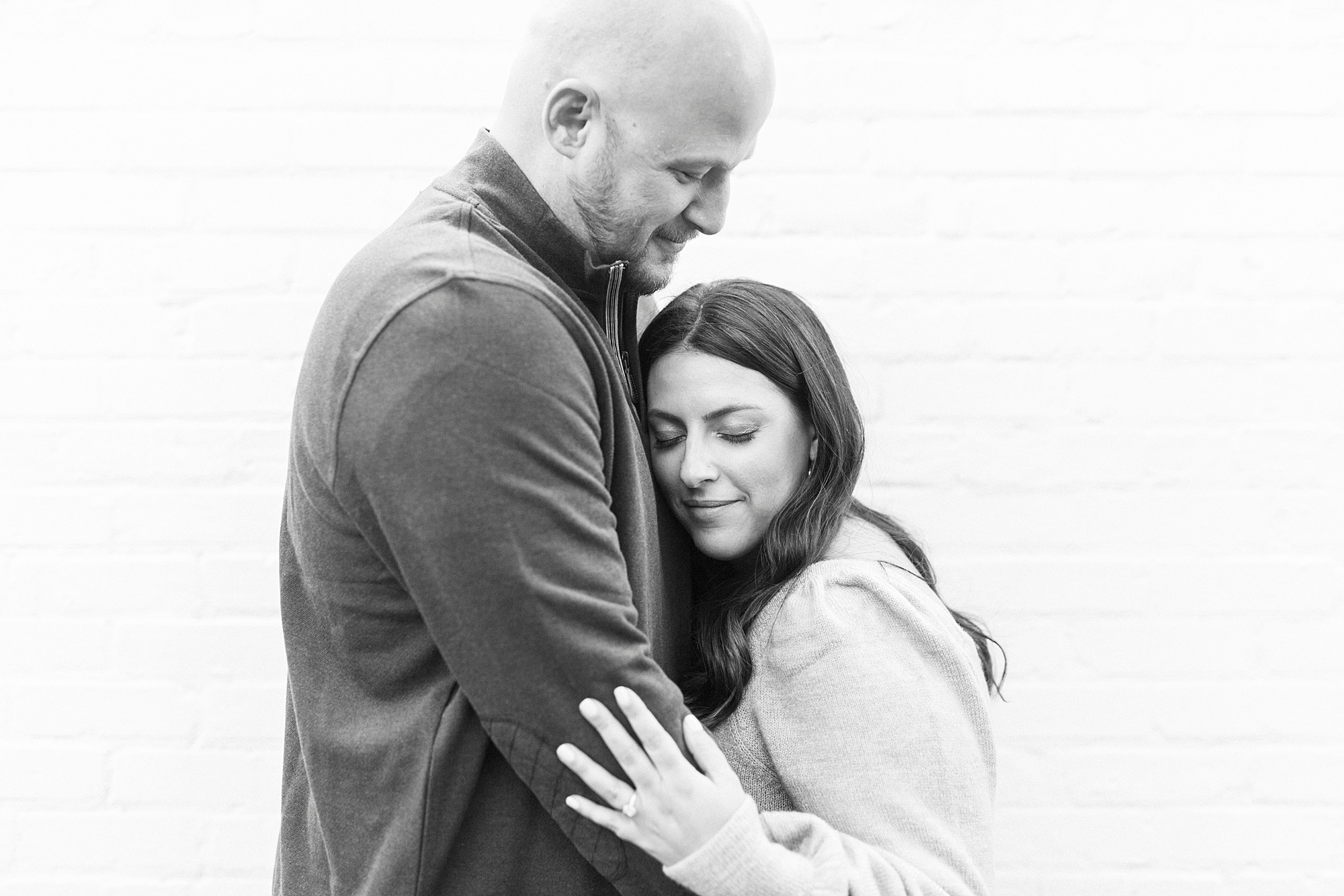 bride leans on groom's chest during NC engagement photos in Downtown Matthews