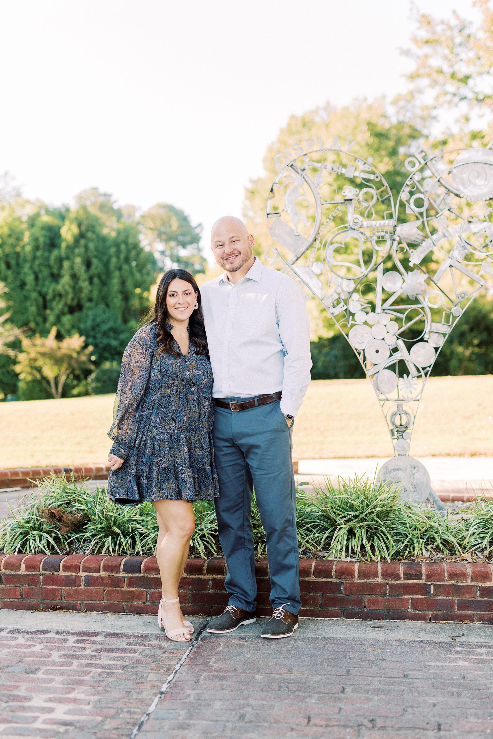 bride and groom pose by statue in garden