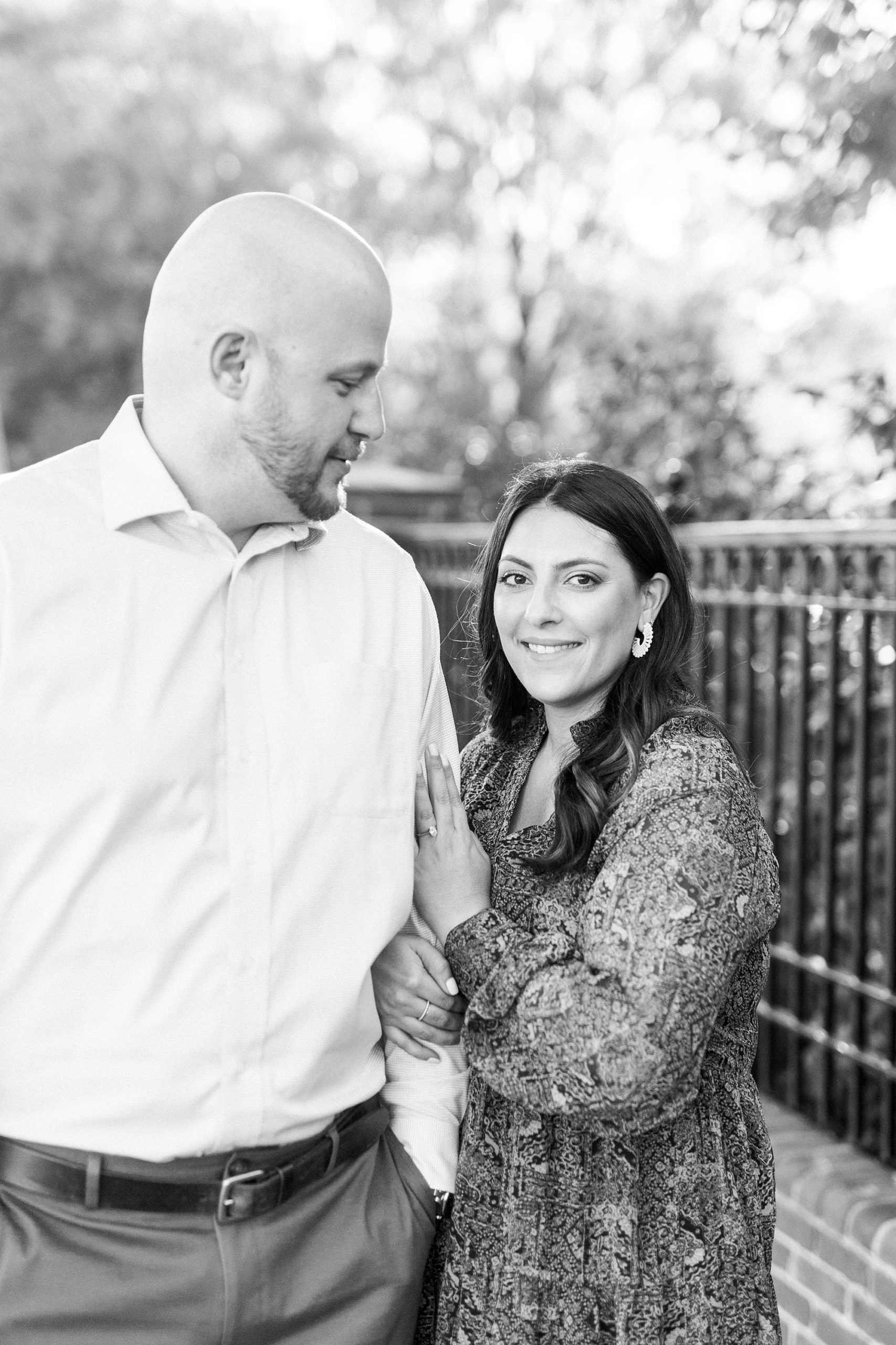 bride holds groom's arm during engagement photos in Downtown Matthews