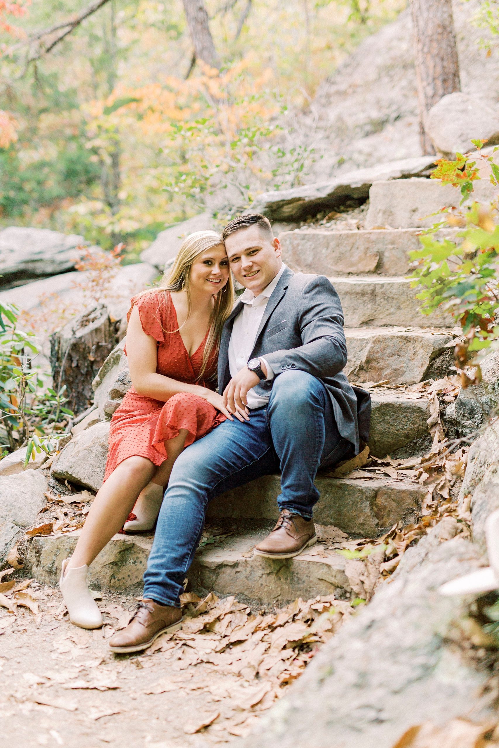 bride and groom sit on stone steps during fall engagement session