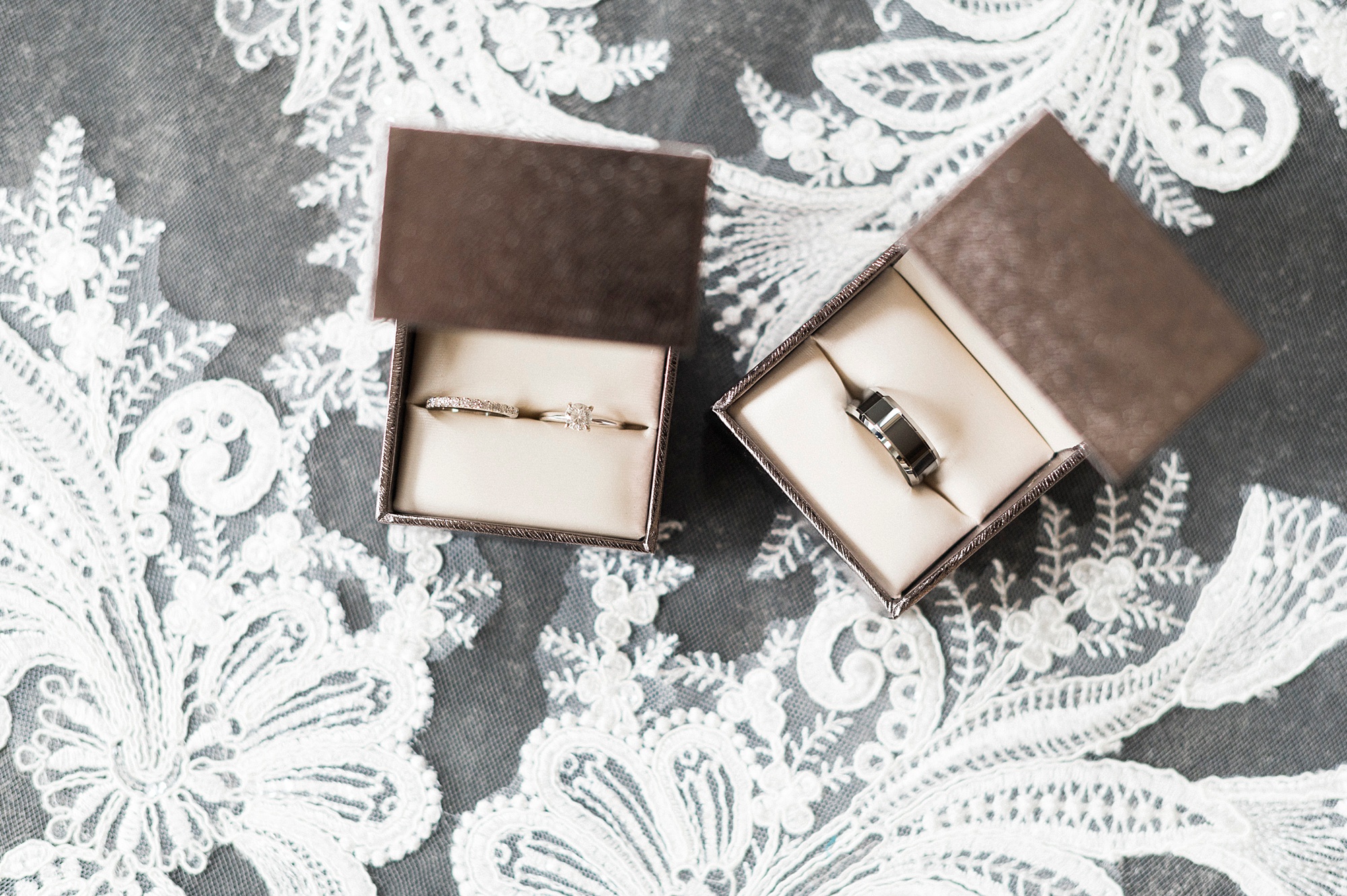 bride's rings in brown boxes lay on lace of veil