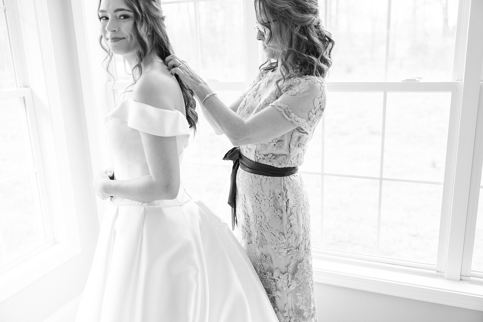 mother helps bride with wedding gown