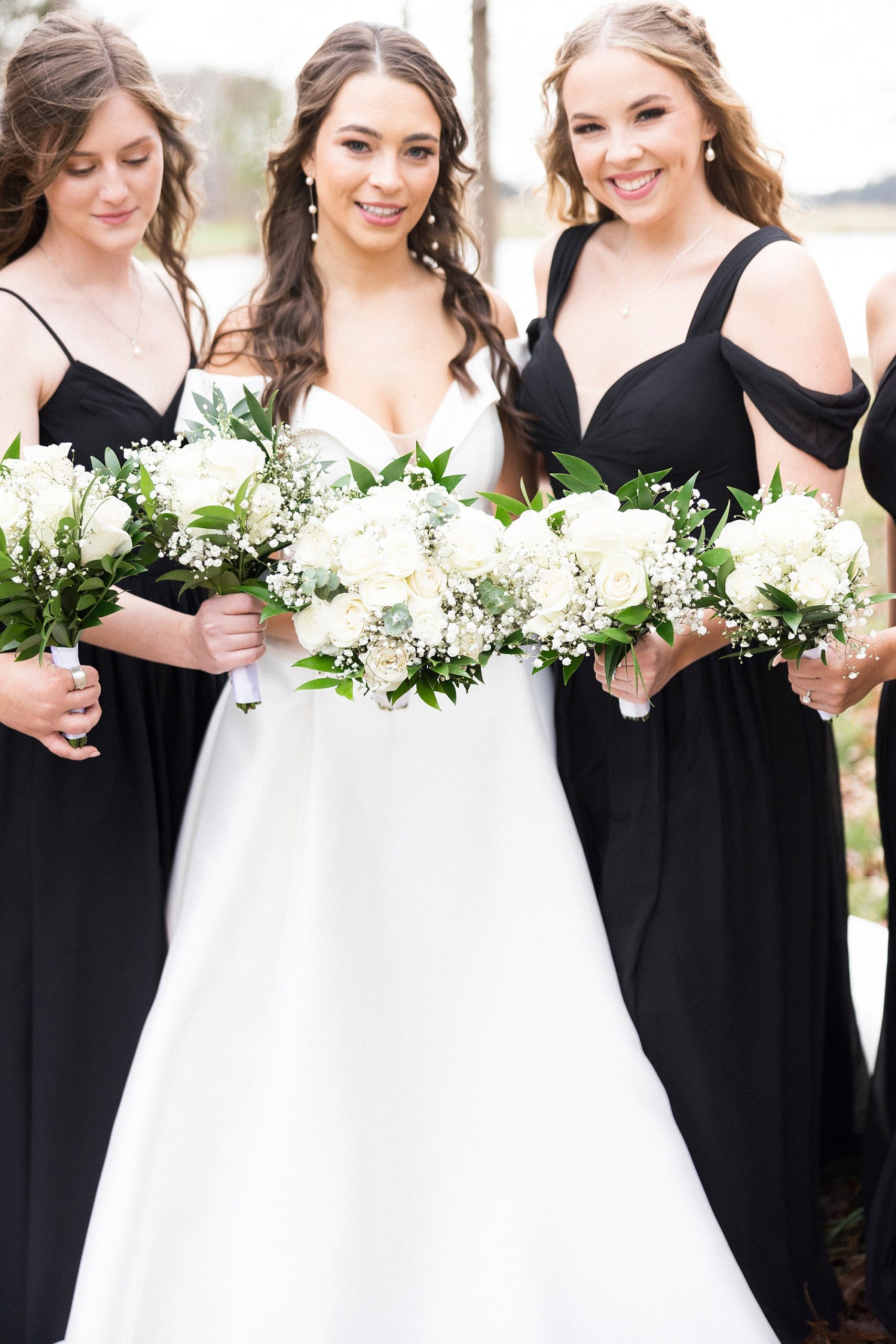 bridesmaids hold all-white bouquets while wearing black gowns