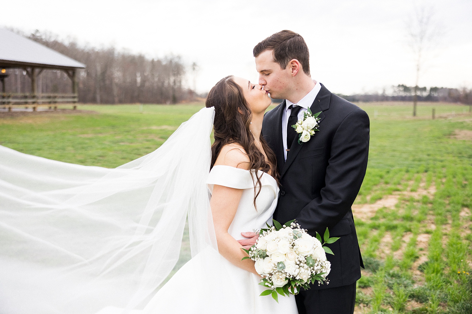 bride and groom kiss with bride's veil floating behind them