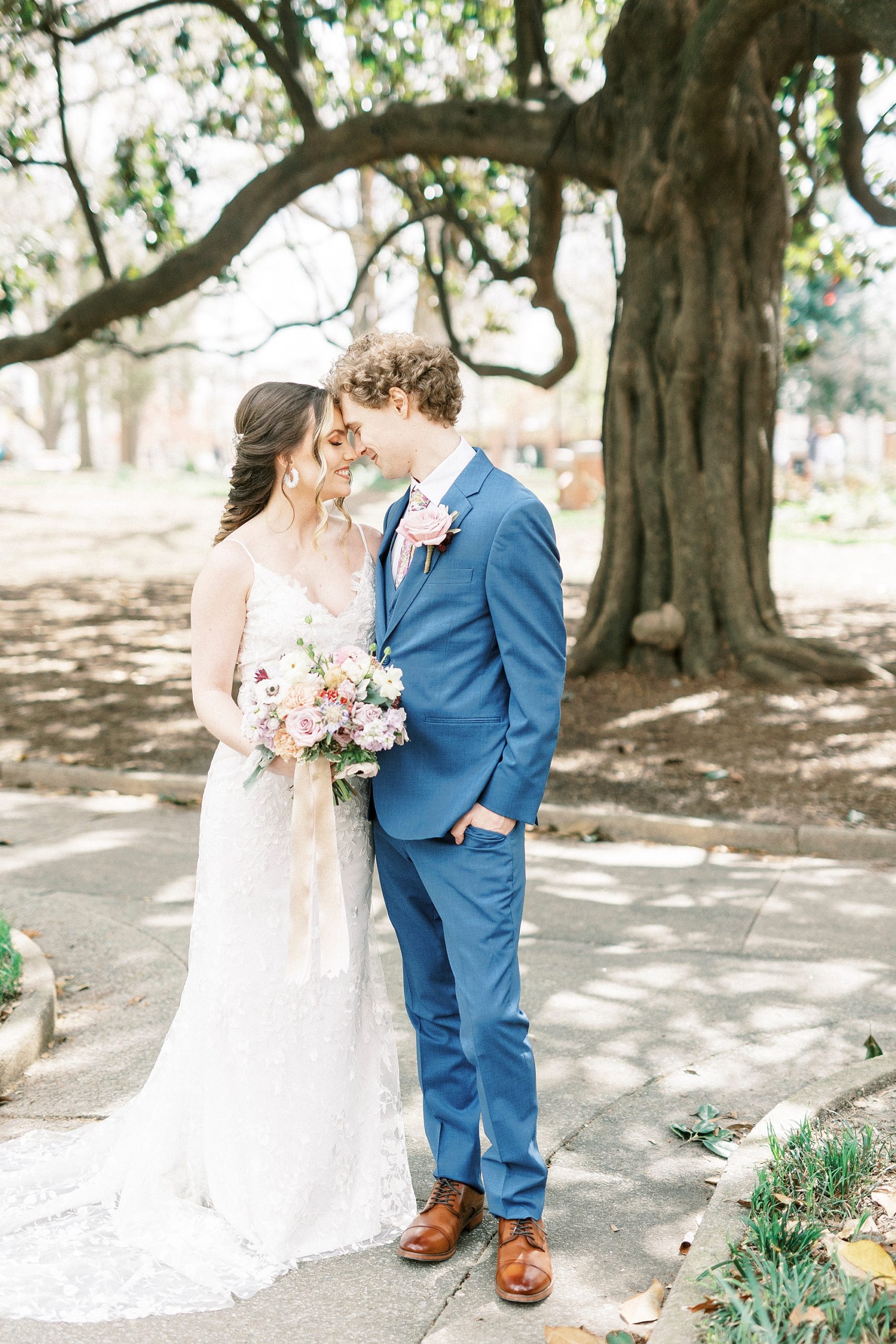 bride and groom stand with heads touching under tree in Raleigh NC