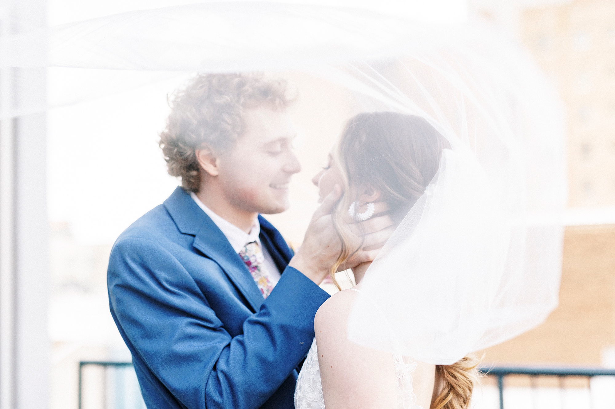 bride and groom stand together under veil