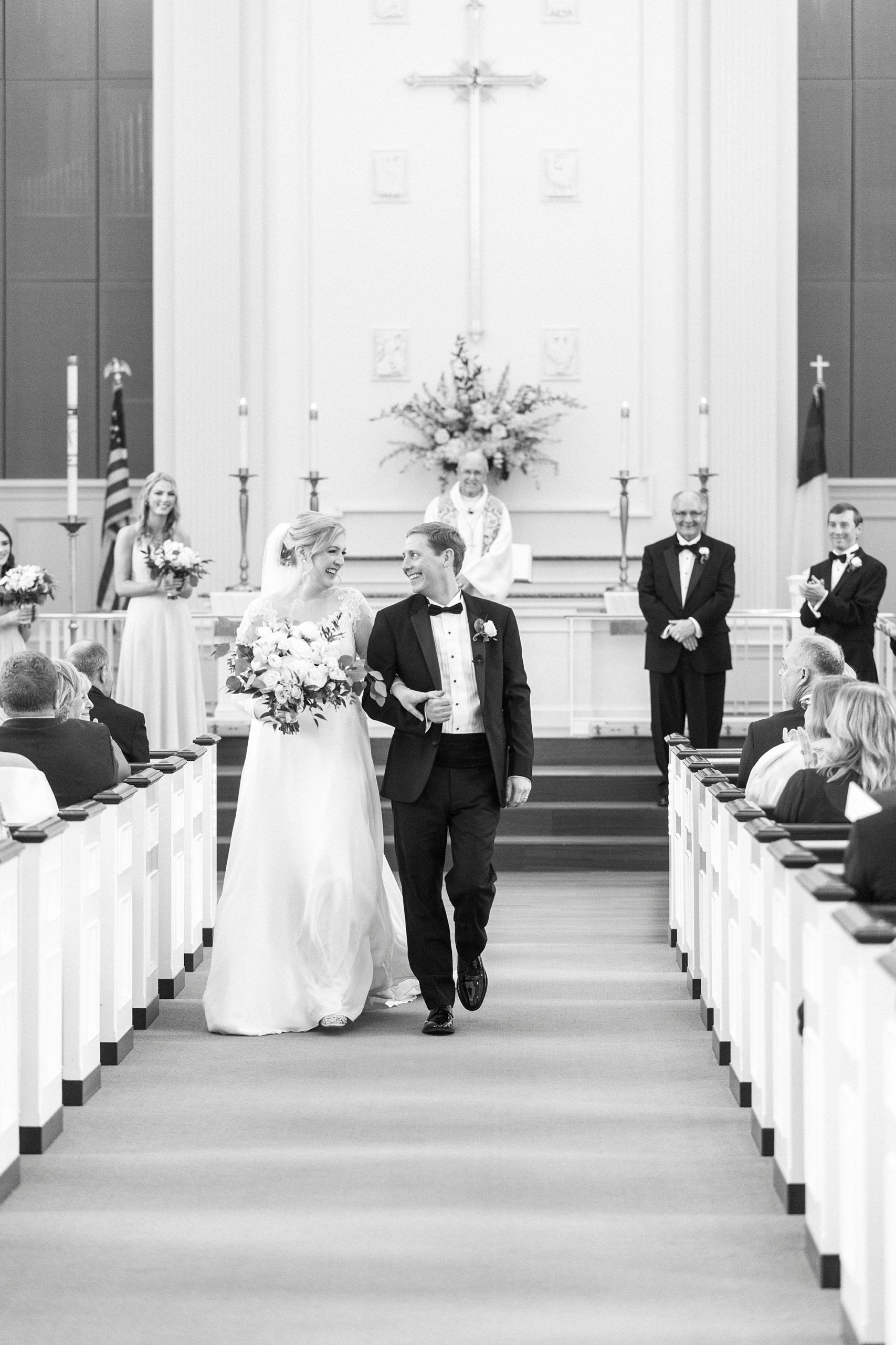 bride and groom smile together walking up aisle 