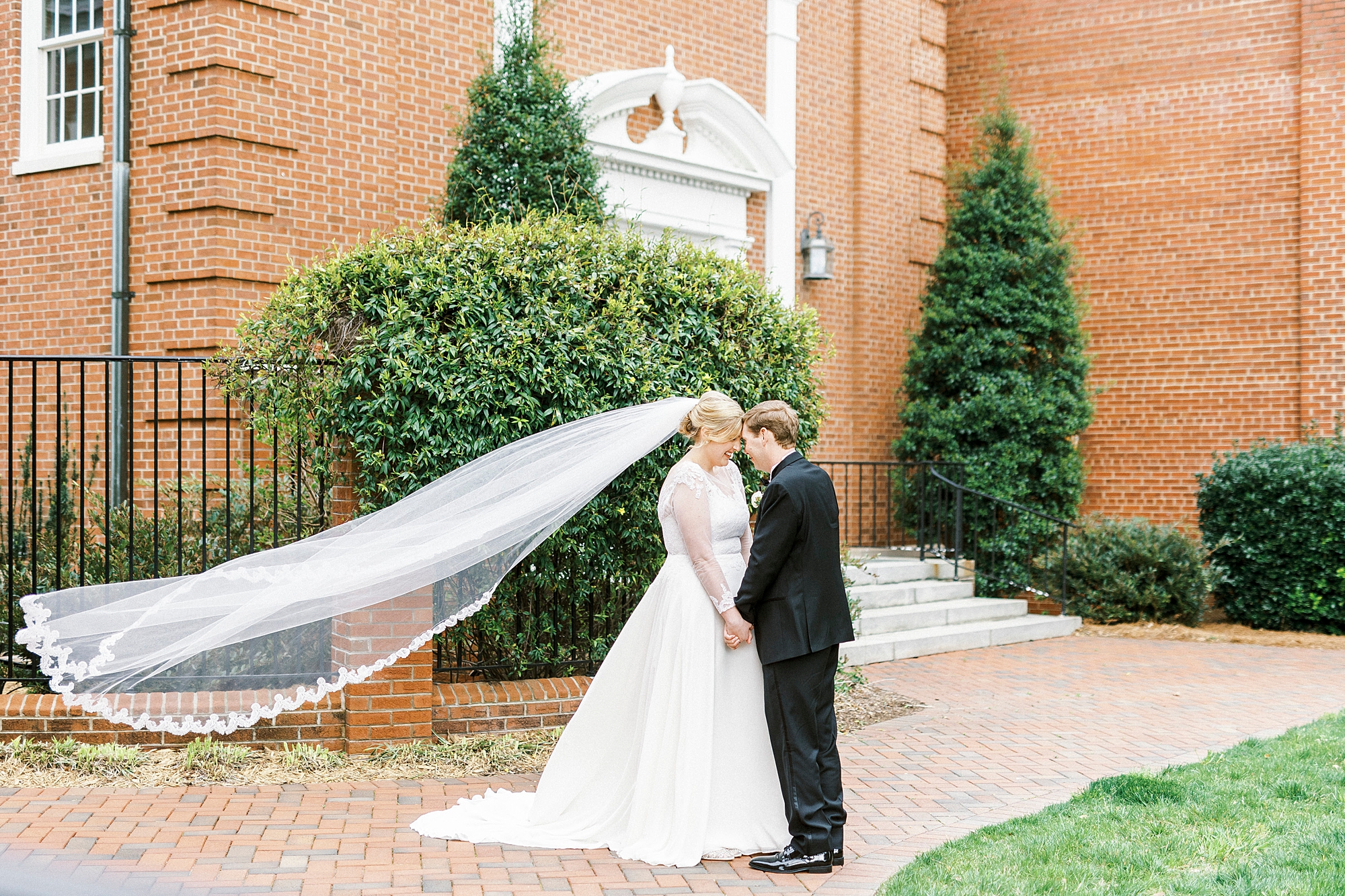 newlyweds lean heads together while bride's veil floats 