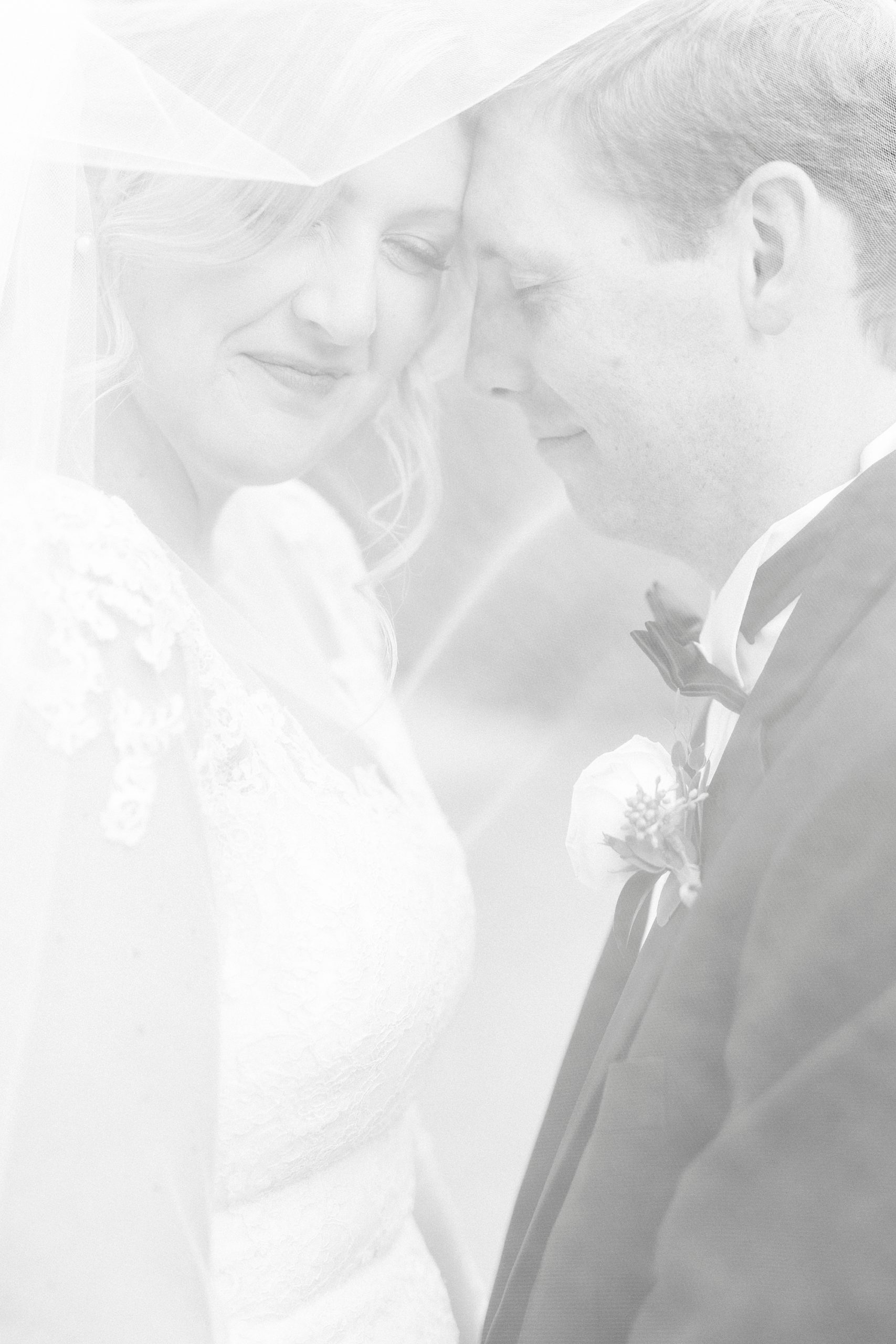newlyweds lean heads together under bride's veil