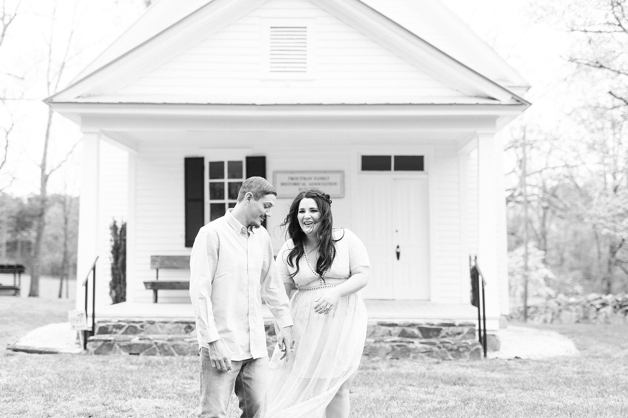 bride and groom laugh on lawn of white chapel