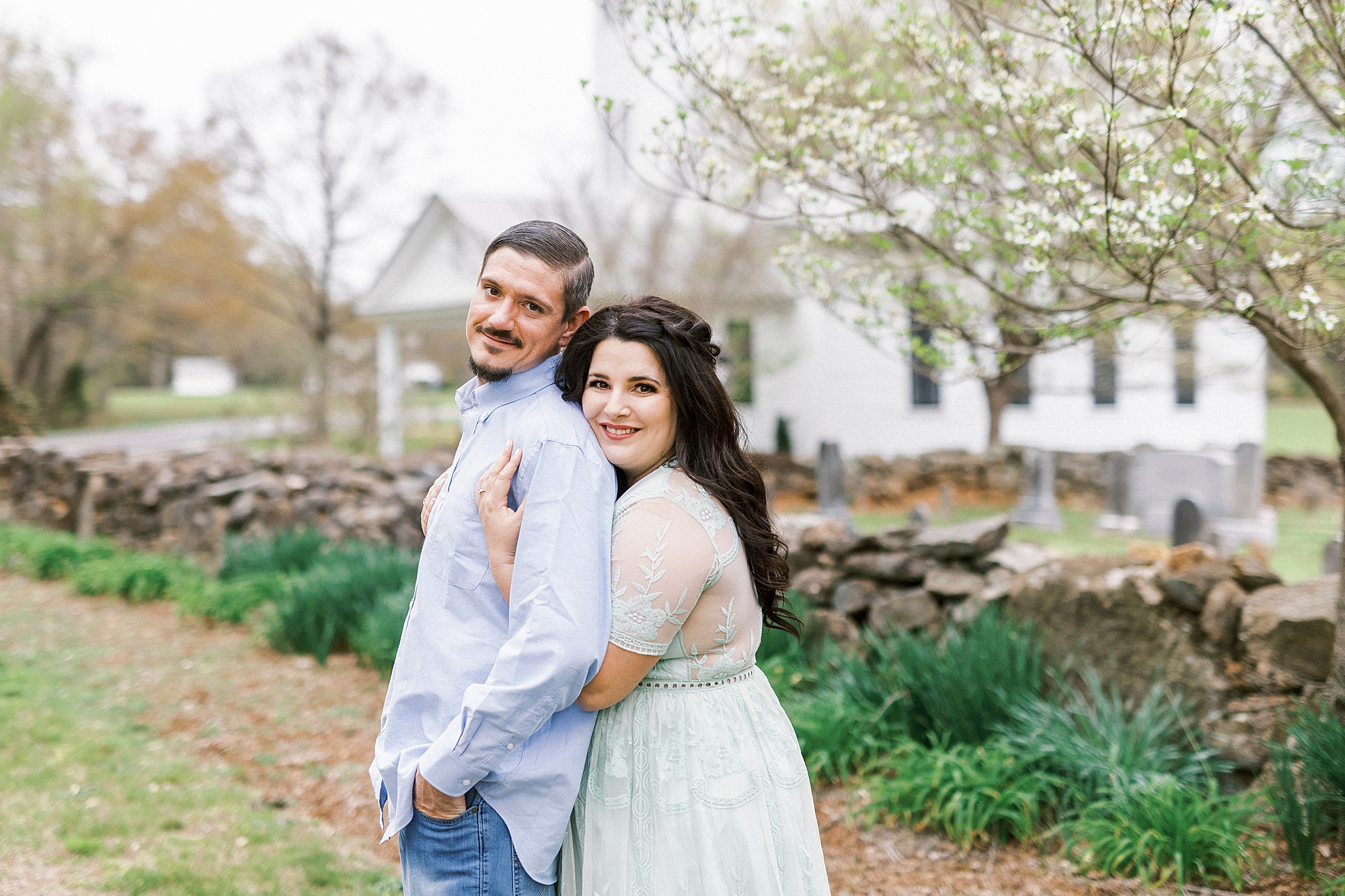 bride hugs groom's shoulders near stone wall