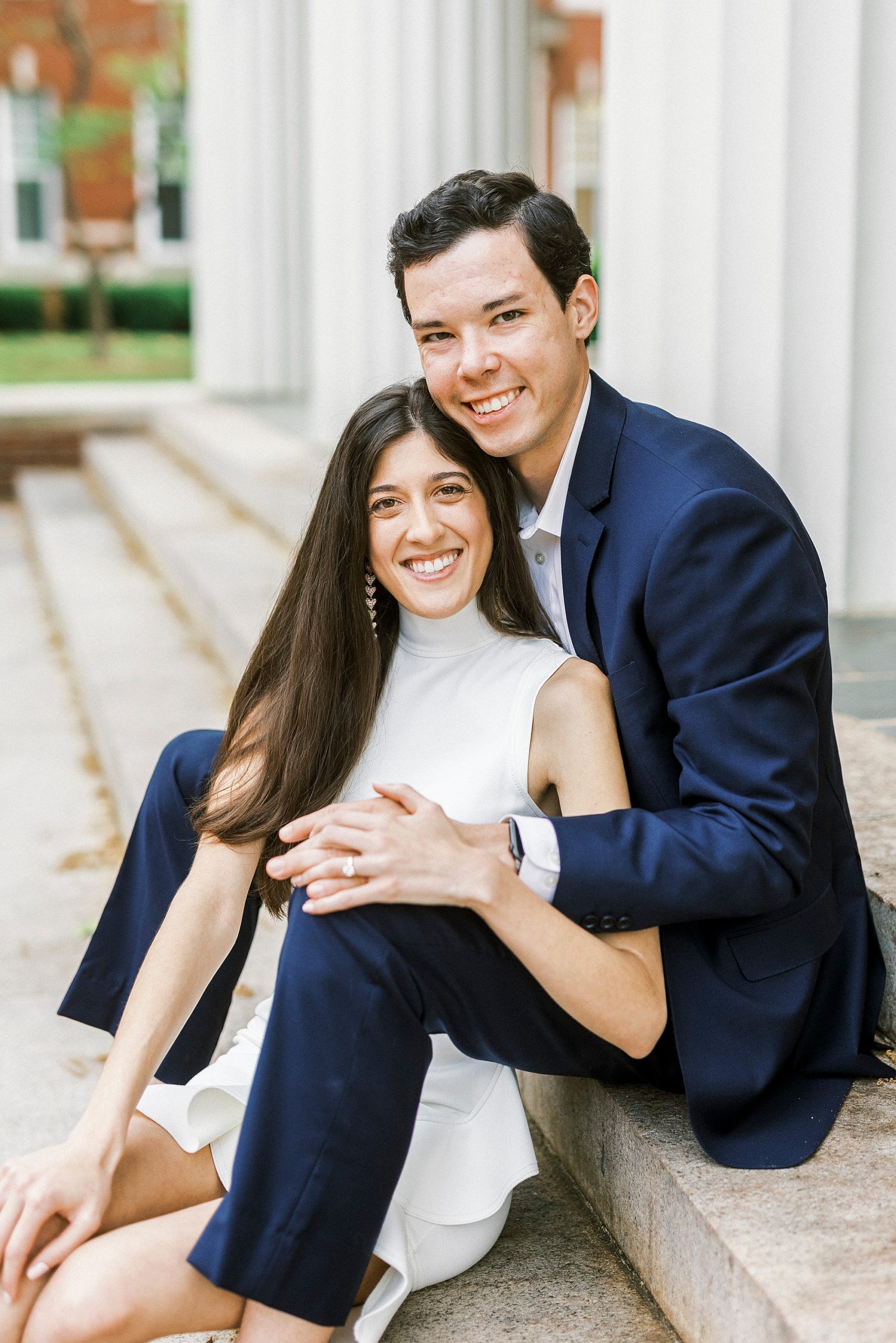 bride leans into groom's chest sitting on steps at Queens University