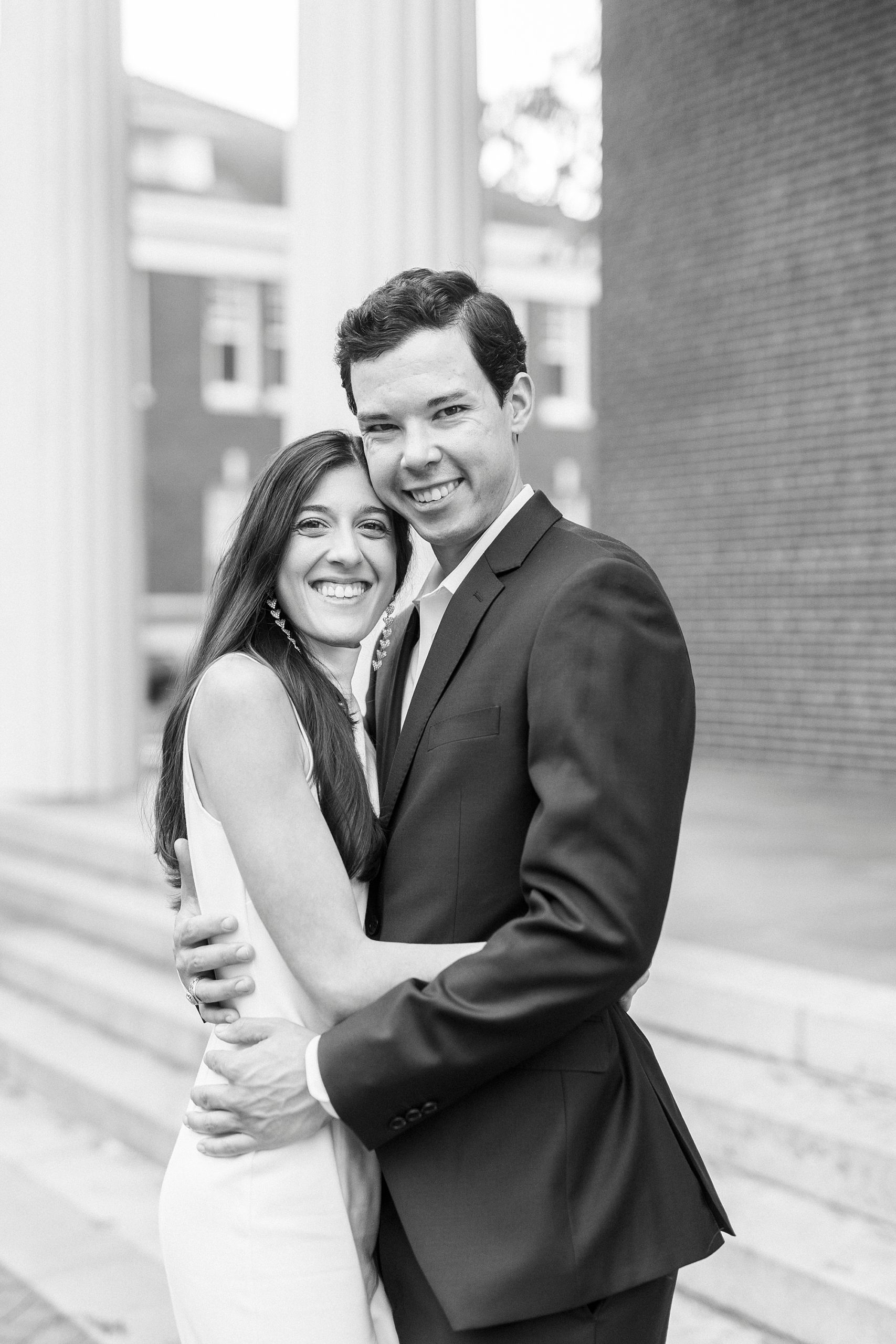 engaged couple hugs outside Queens University building