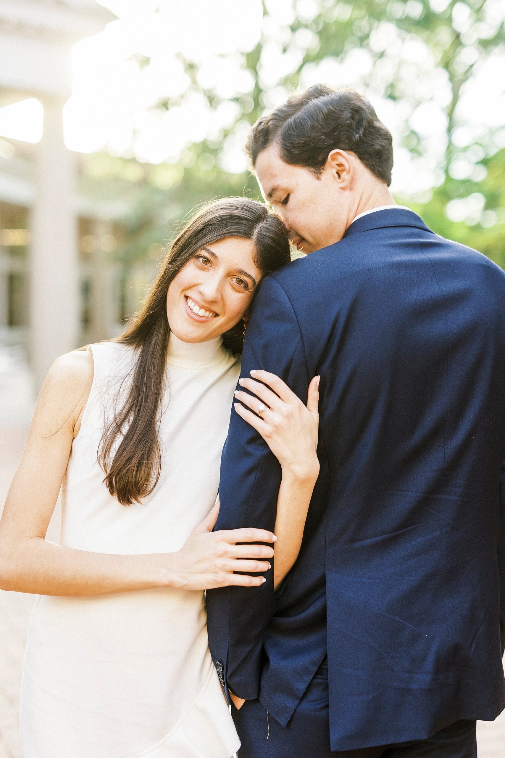 bride leans on groom's arm showing off engagement ring