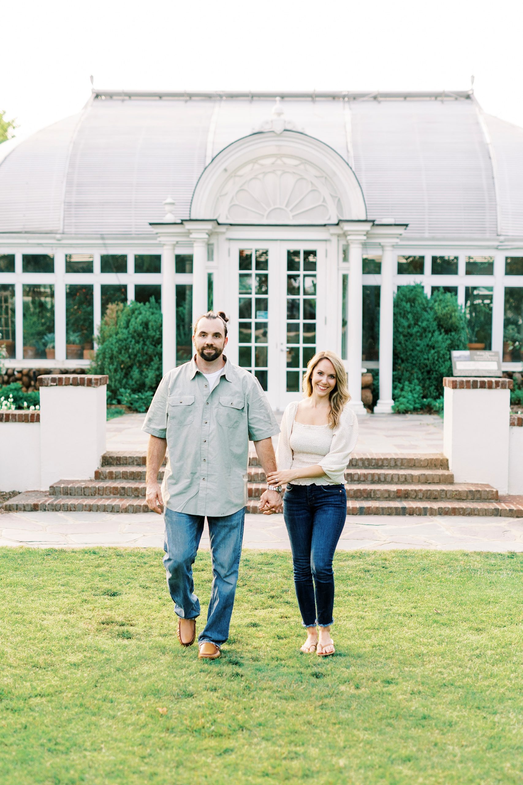 engaged couple hold hands walking across lawn at Reynolda Gardens
