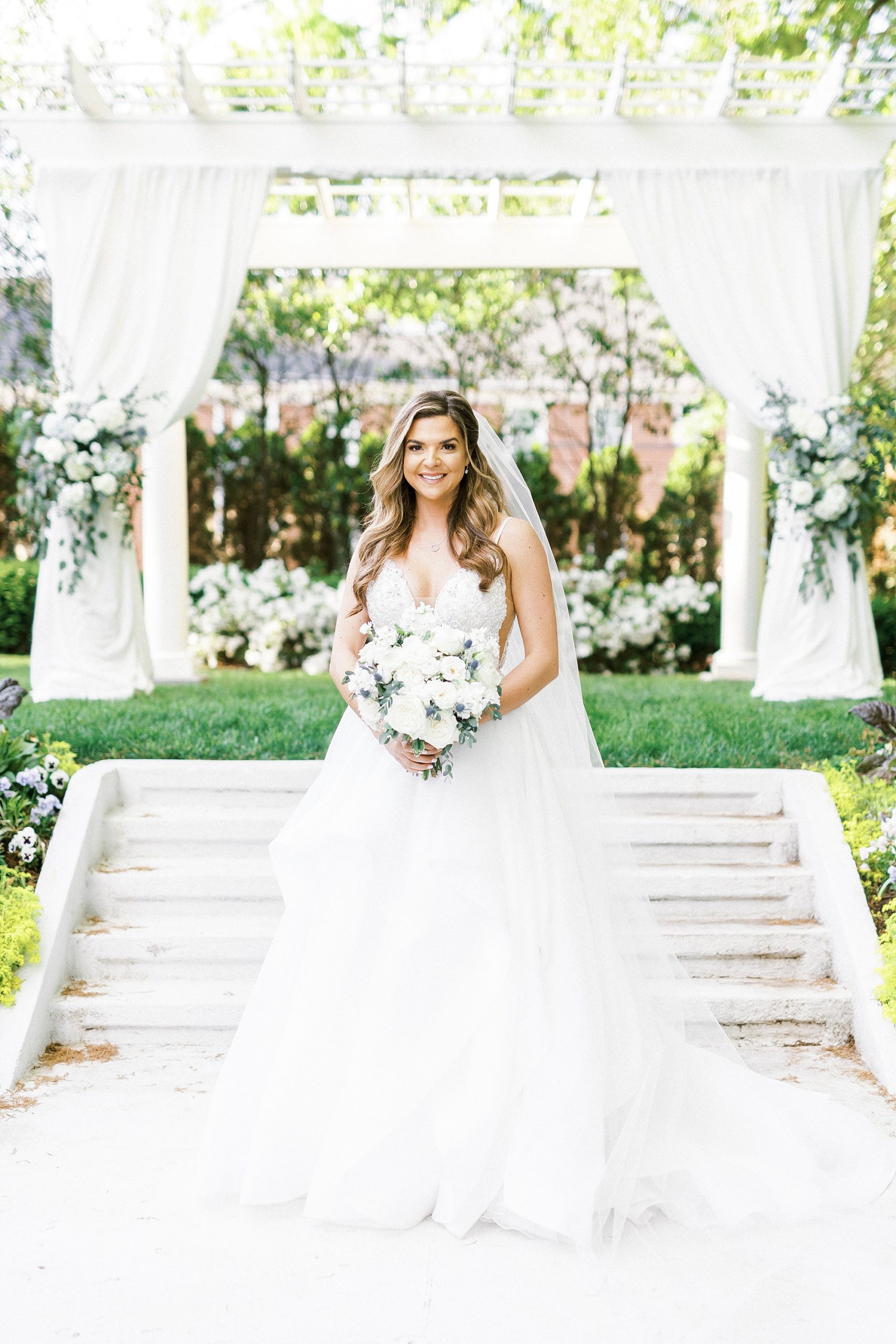 bride poses with bouquet of all white flowers for spring wedding day
