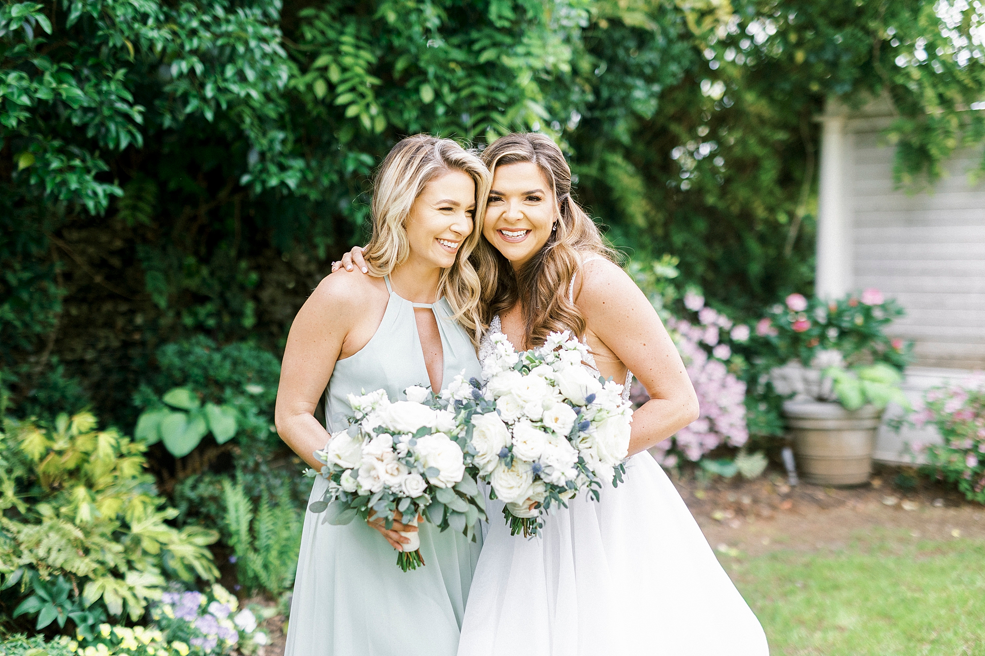 bride hugs bridesmaid holding all white bouquet 