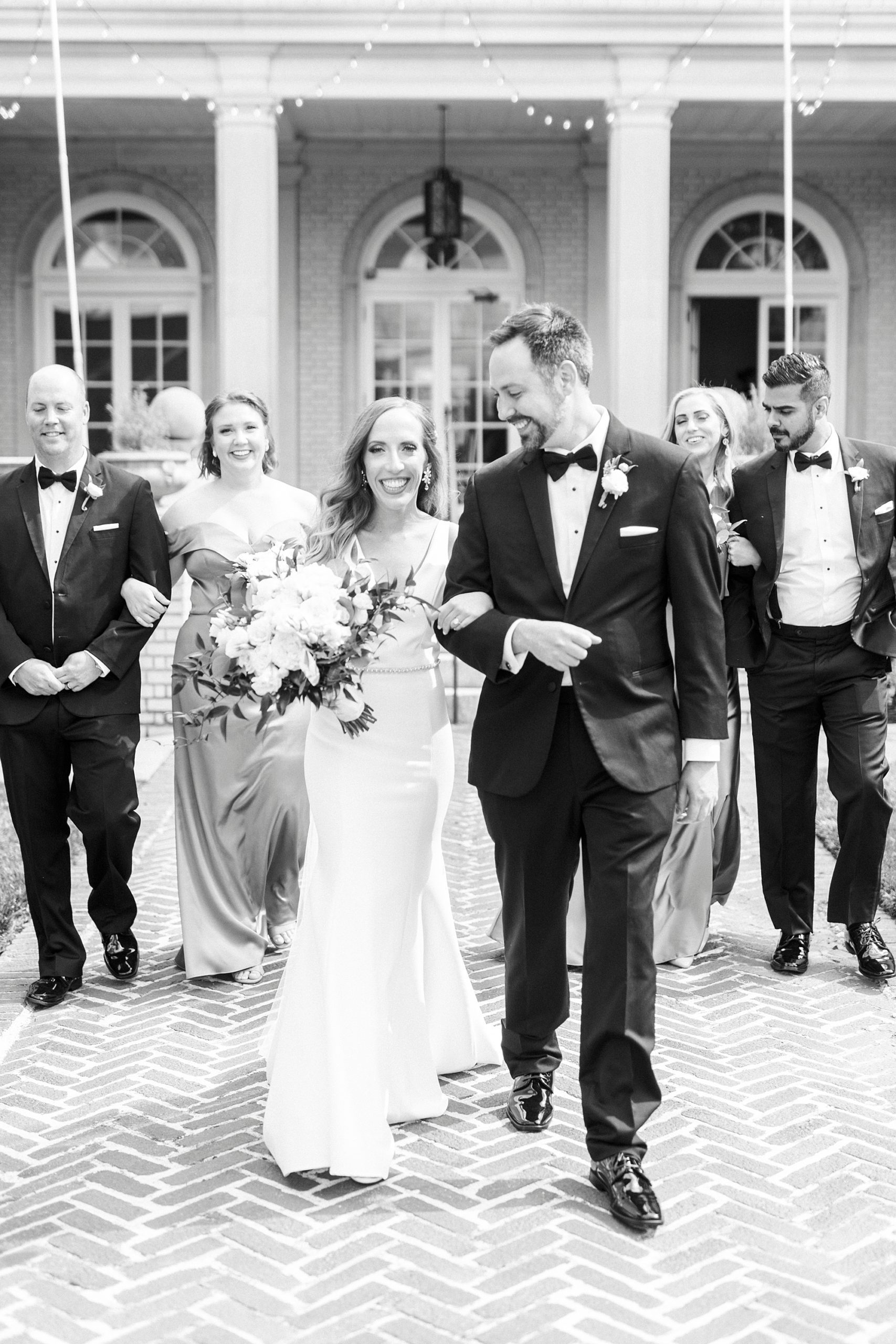 groom looks over at bride walking in front of bridal party outside Separk Mansion