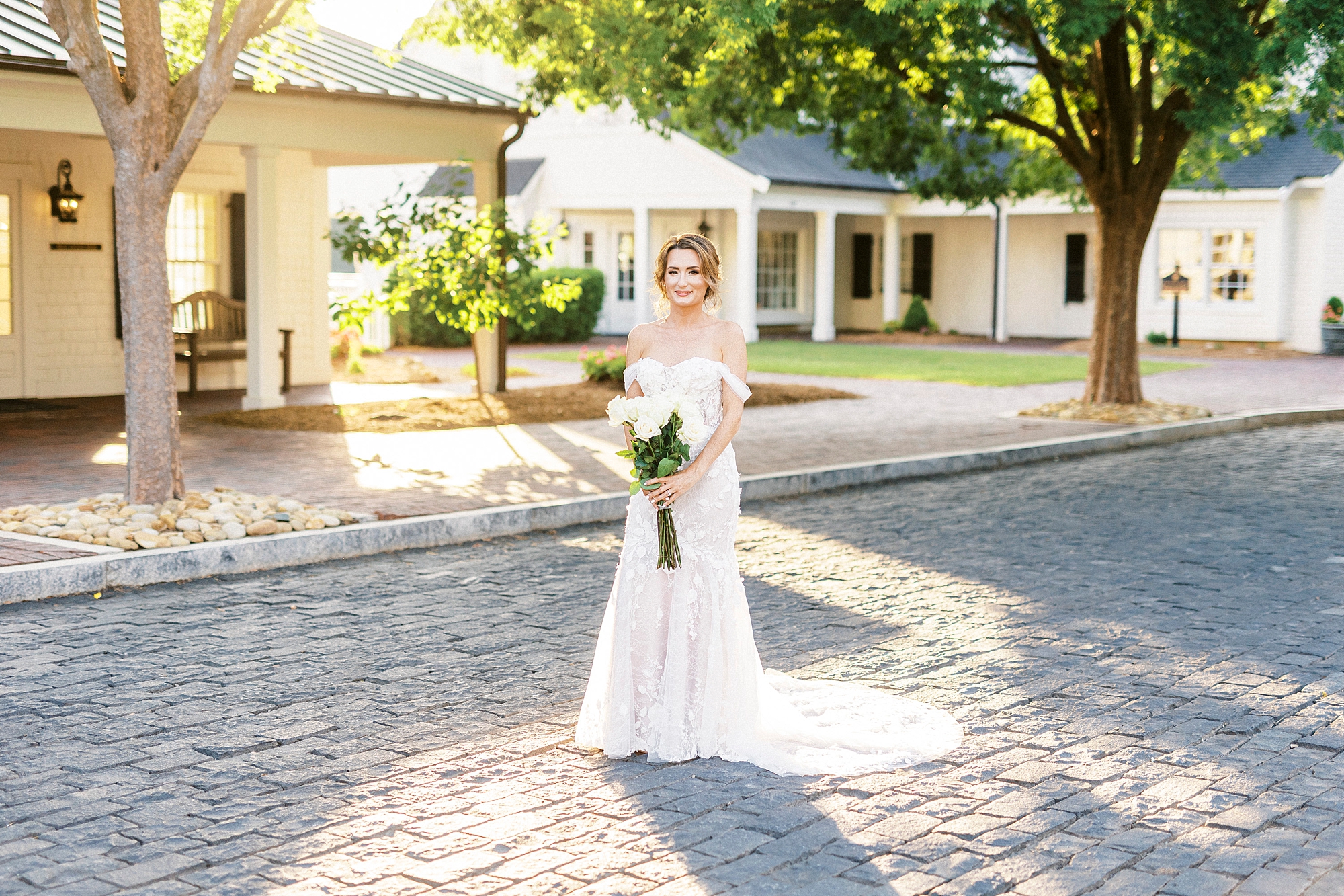 bride poses outside Trump National Golf Club with bouquet of white flowers 