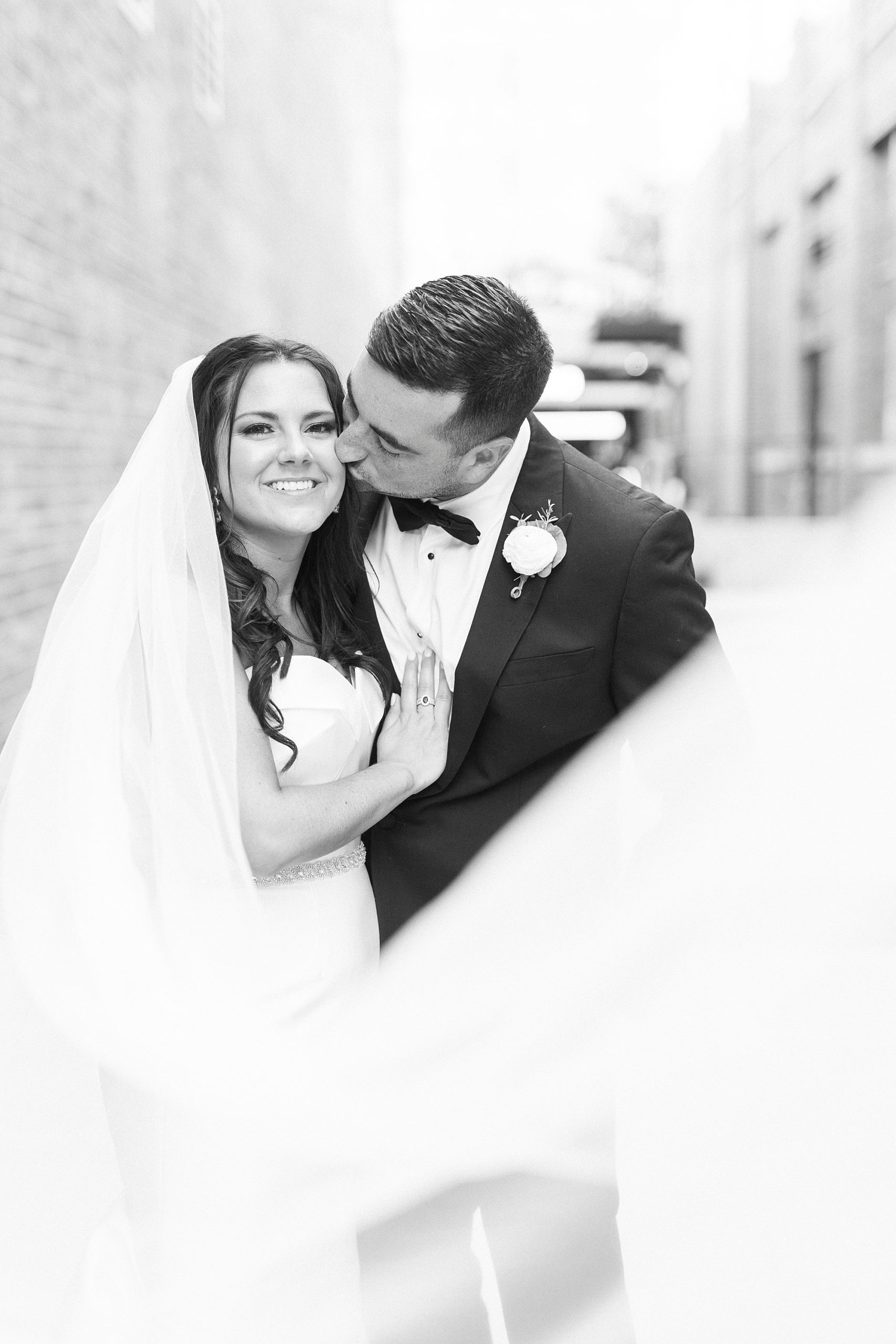 groom leans to kiss bride's cheek with veil around them at Byron's South End