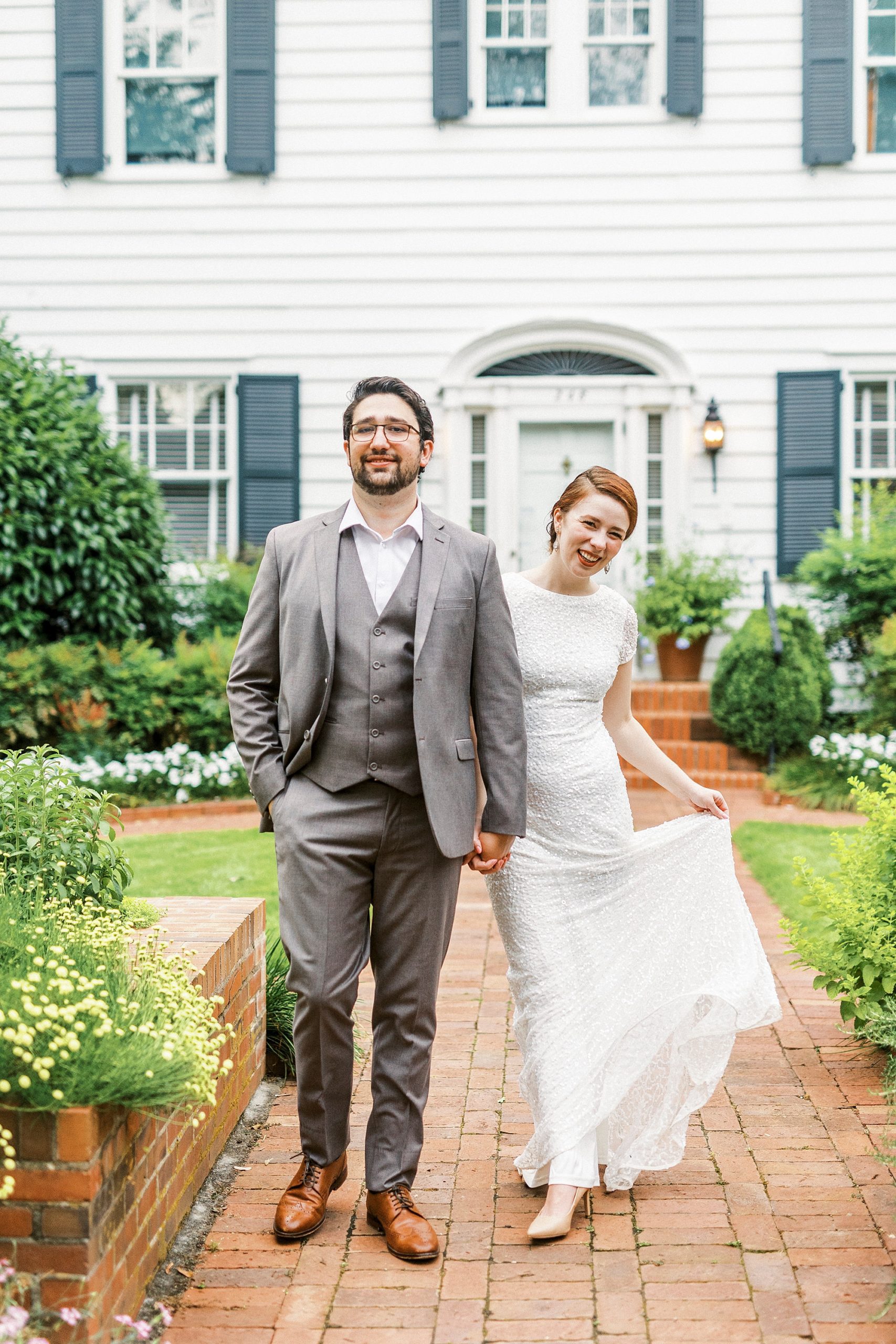 couple holds hands walking down brick walkway 