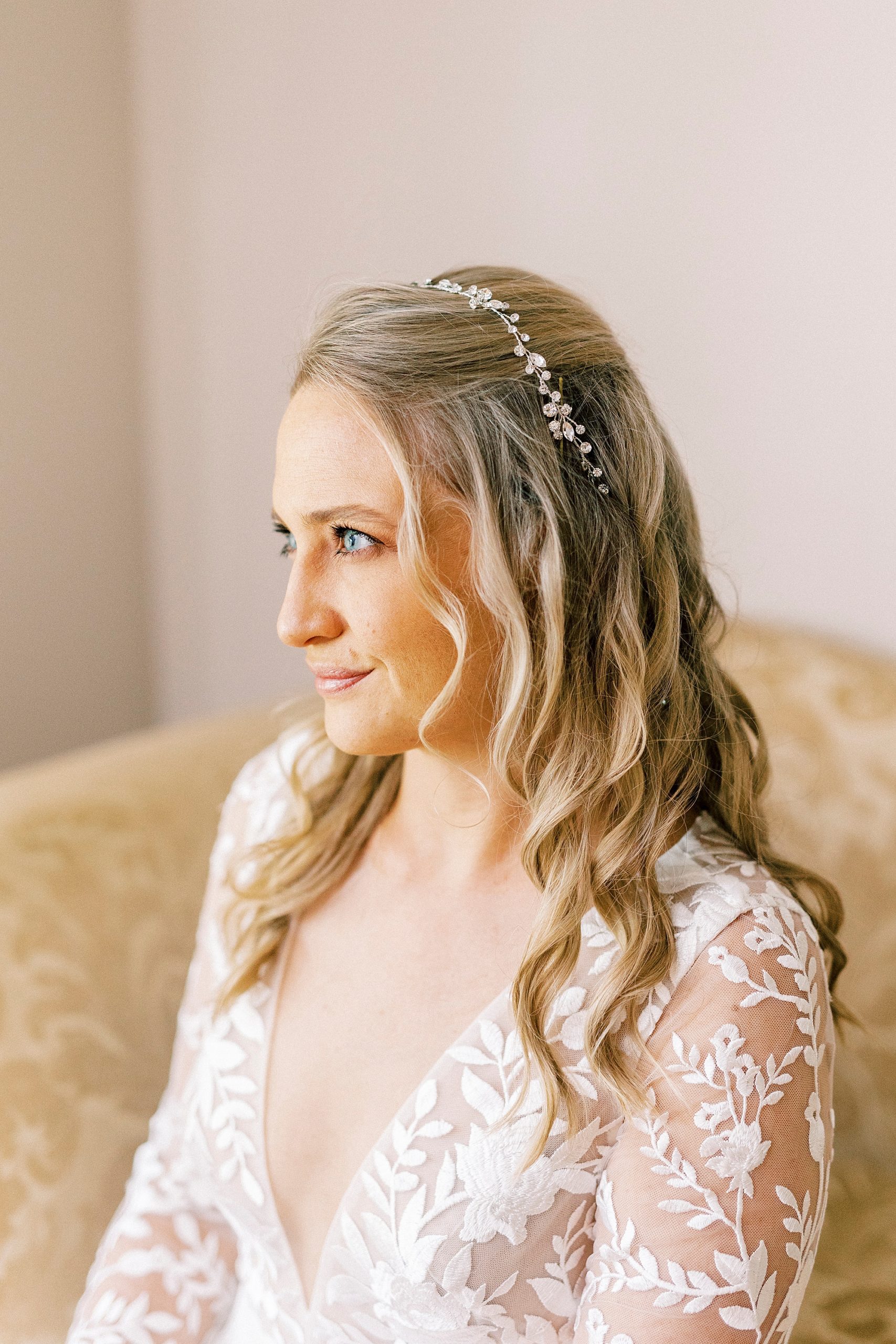 bride looks out window with simple headband sitting on couch 
