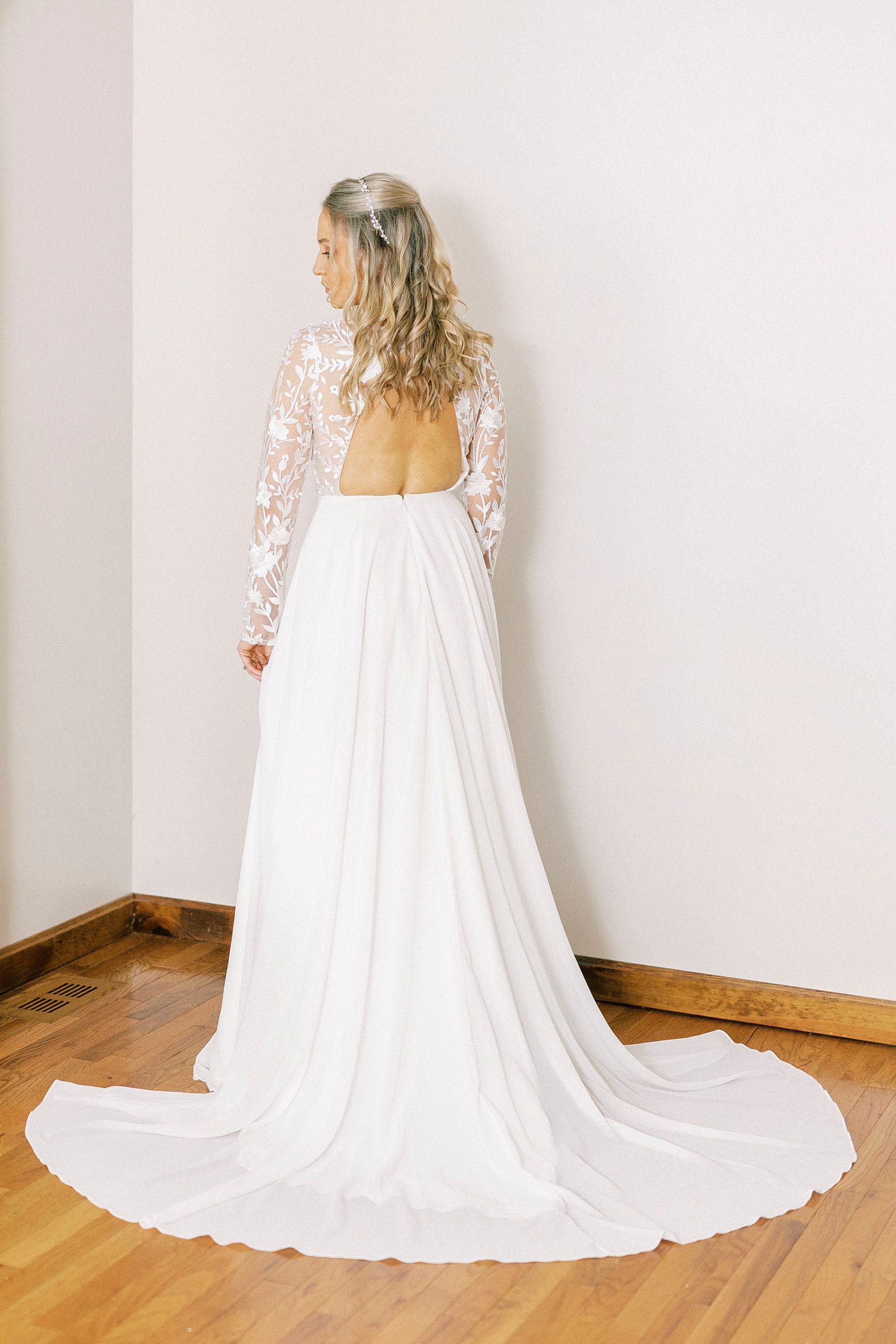 bride stands showing off back of wedding gown with lace bodice 