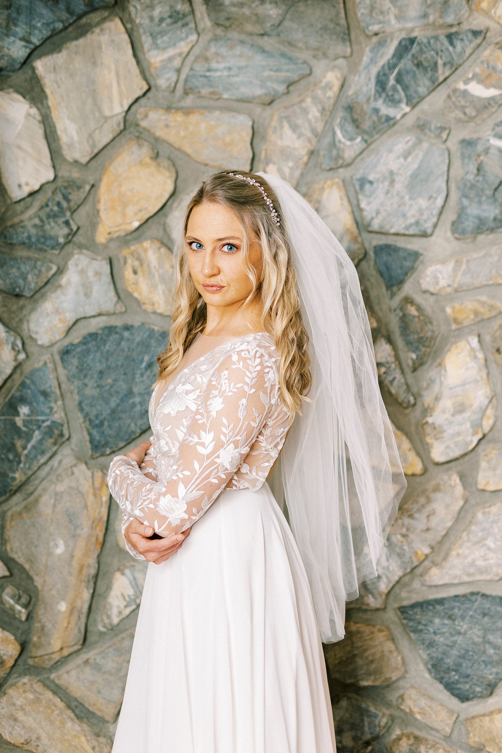 bride looks over shoulder in front of stone wall