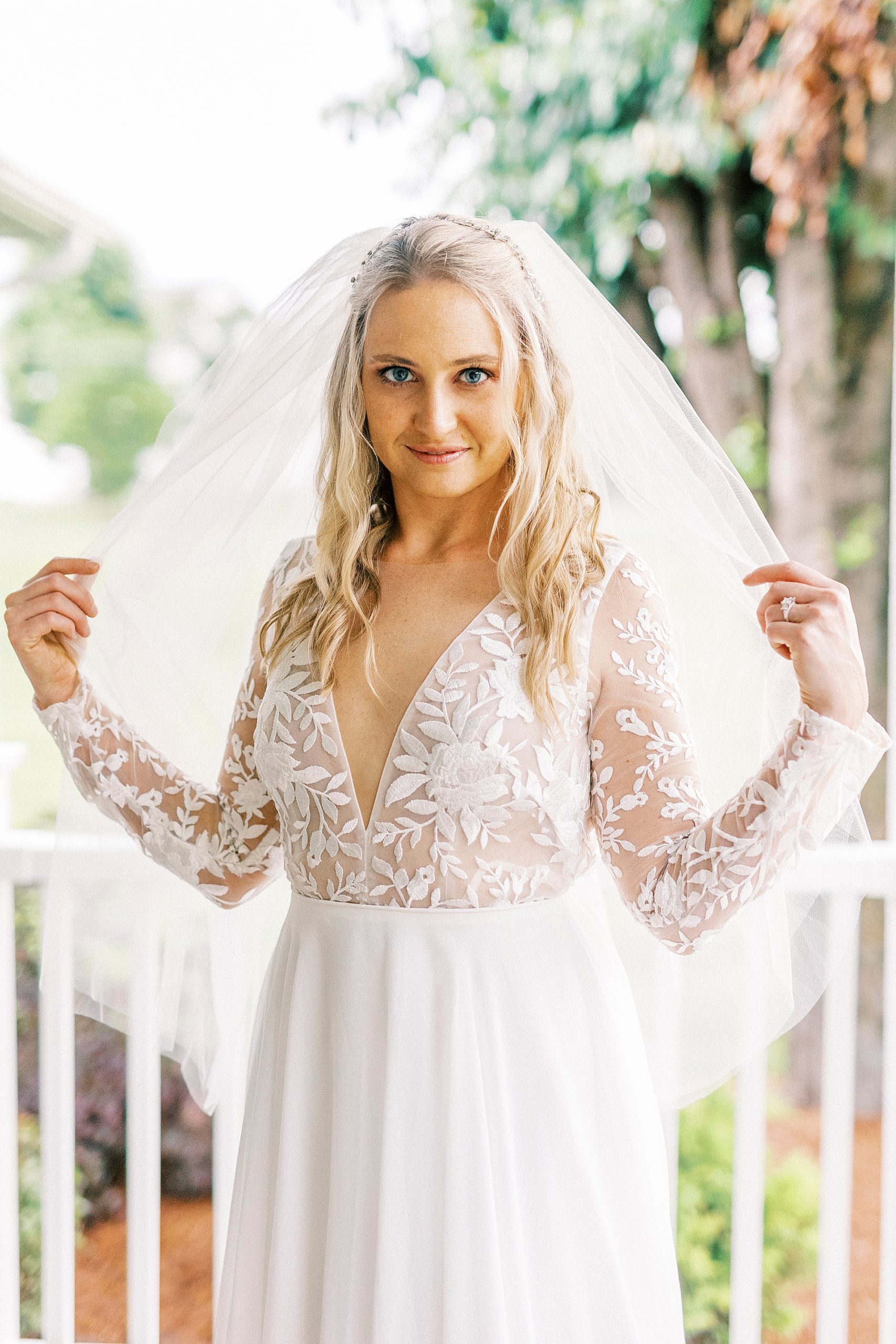 bride pulls veil around shoulders during elegant bridal portraits on front porch