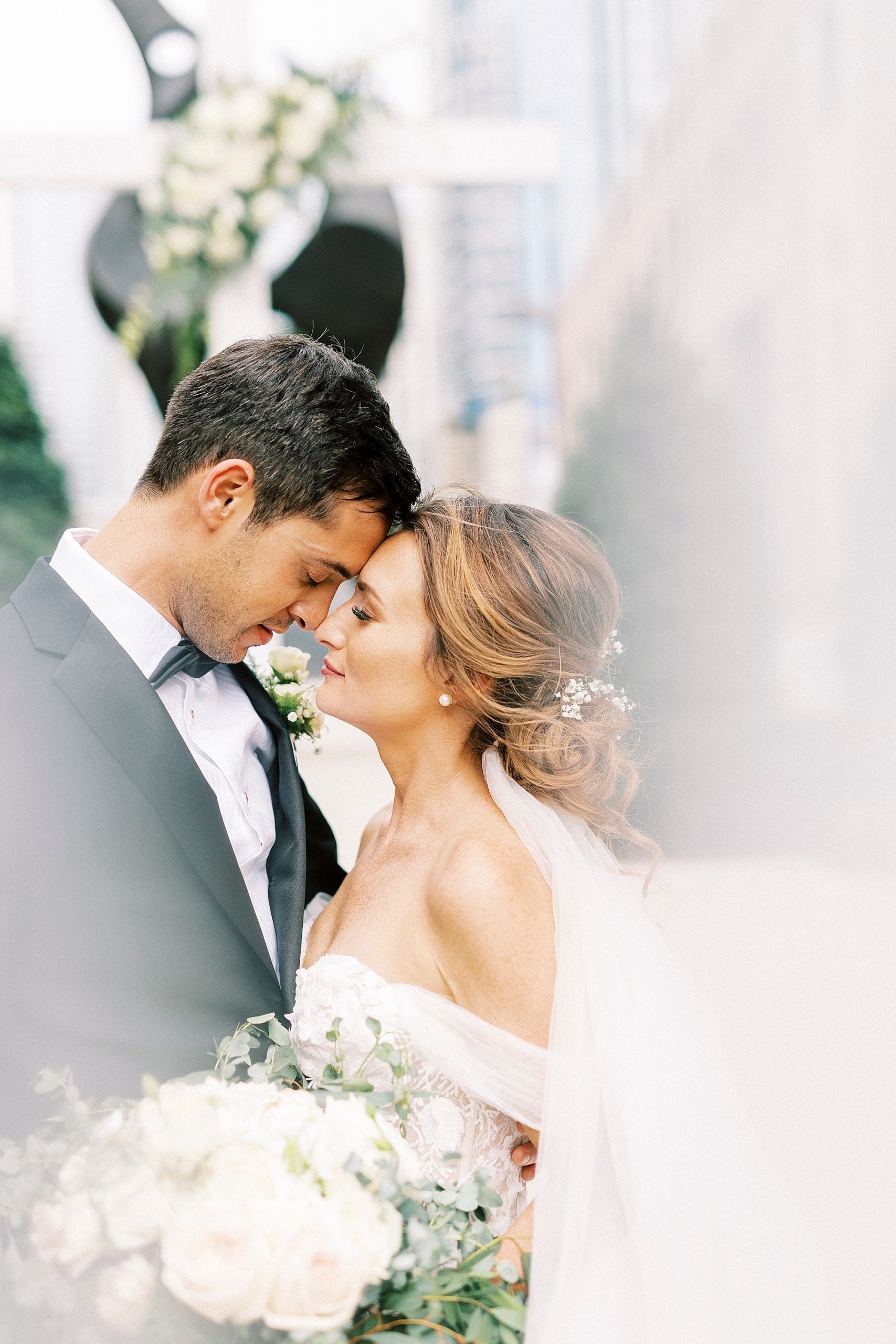 bride and groom touch noses together with veil behind them