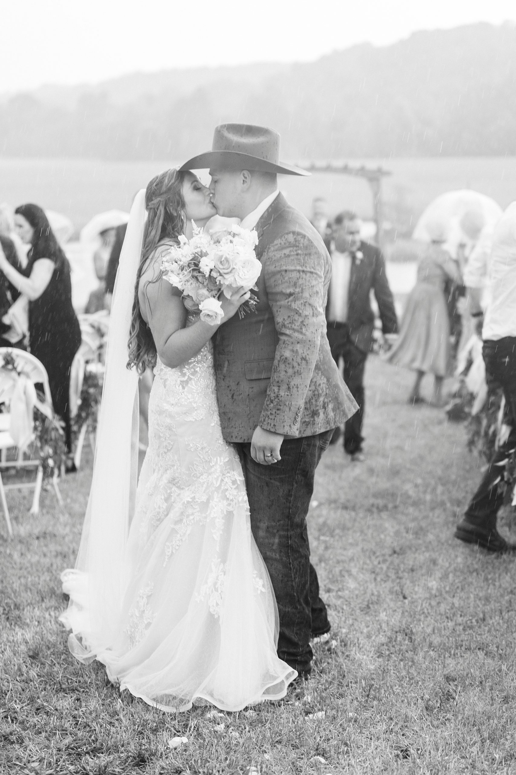 newlyweds kiss at end of aisle after rainy wedding ceremony at The Stable at Riverview
