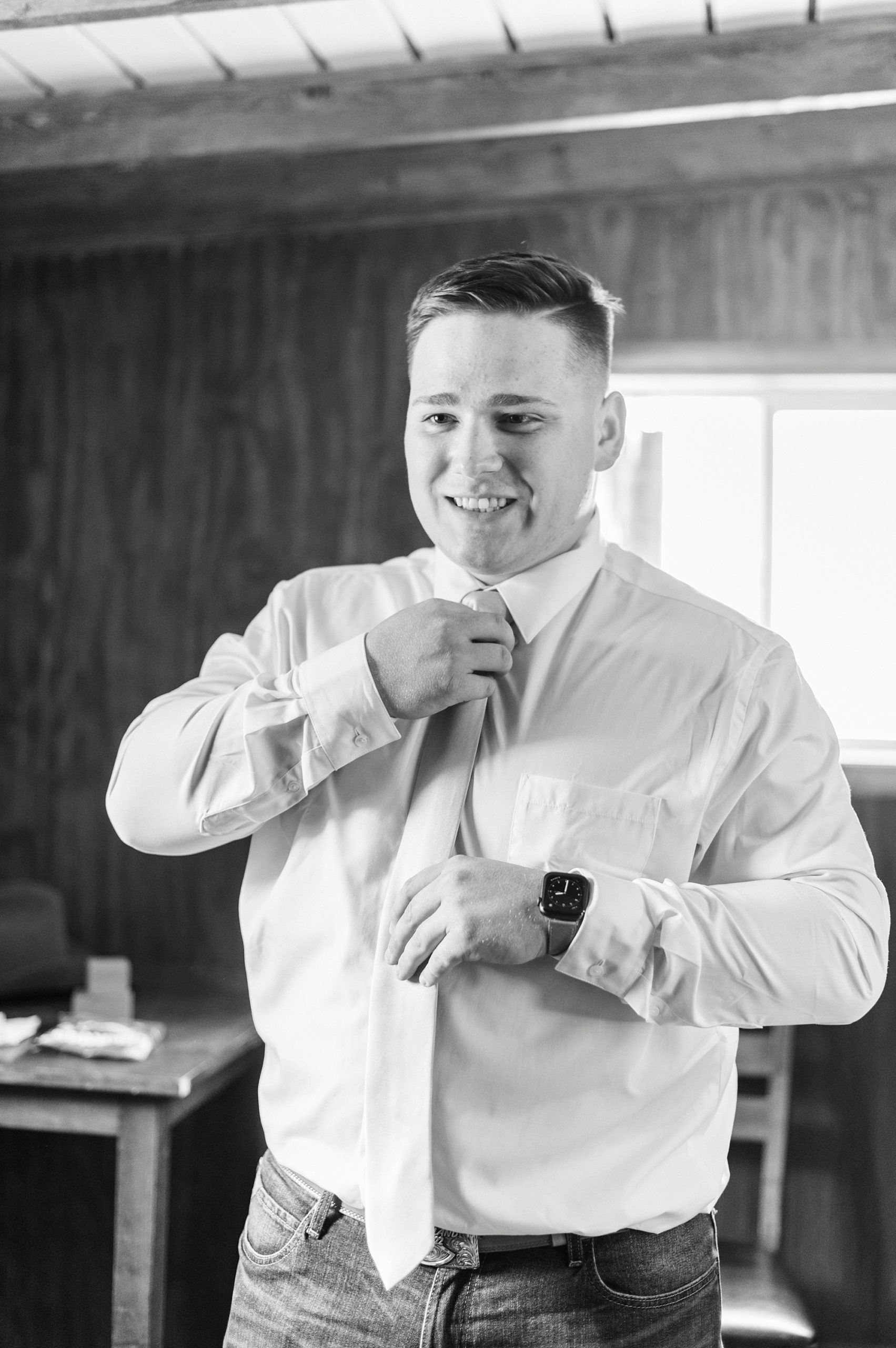 groom adjusts tie during prep for The Stable at Riverview wedding