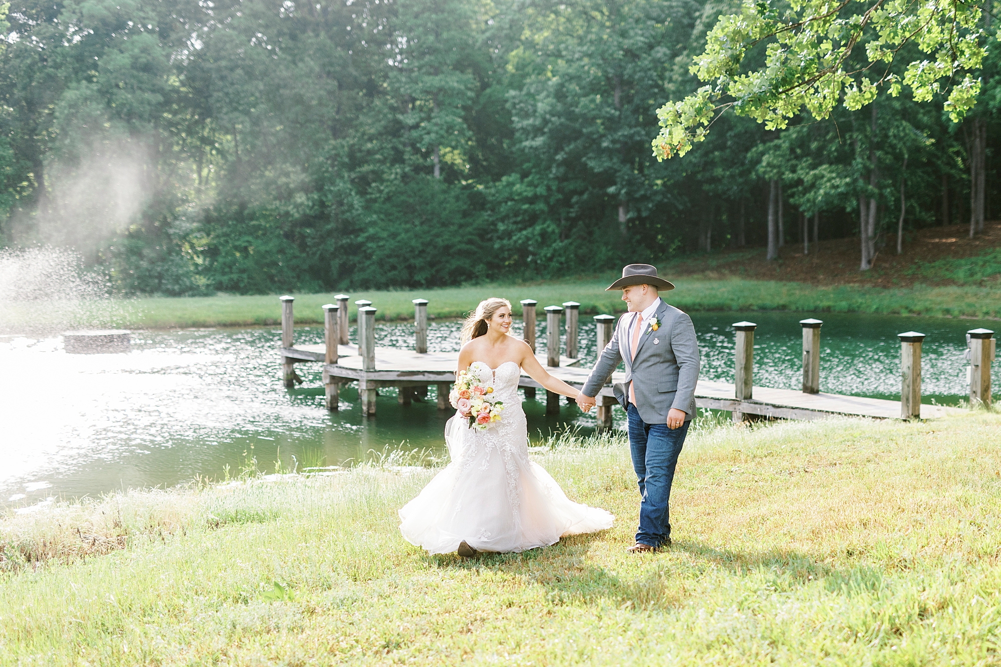 couple holds hands walking alongside pond at The Stable at Riverview