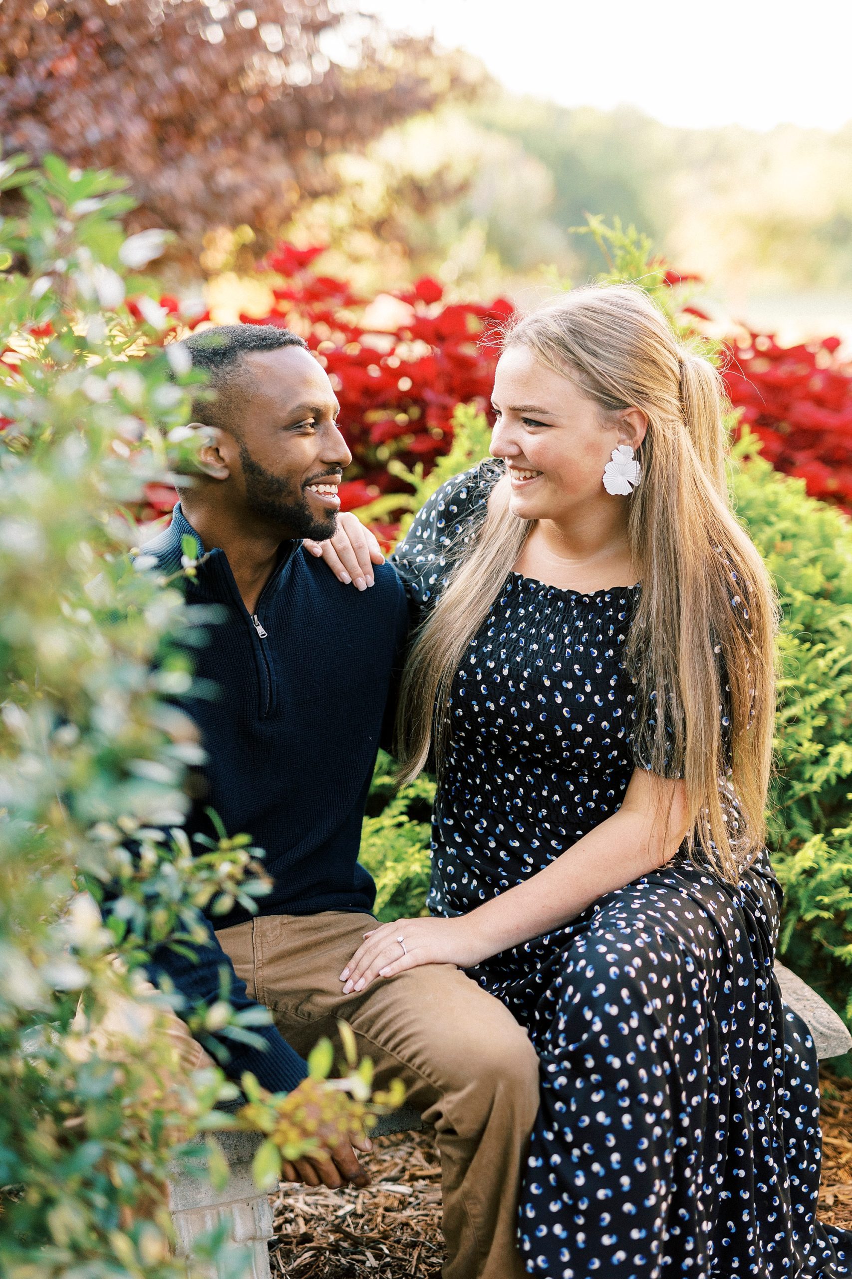 couple laughs sitting among red flowers at Bella Terra