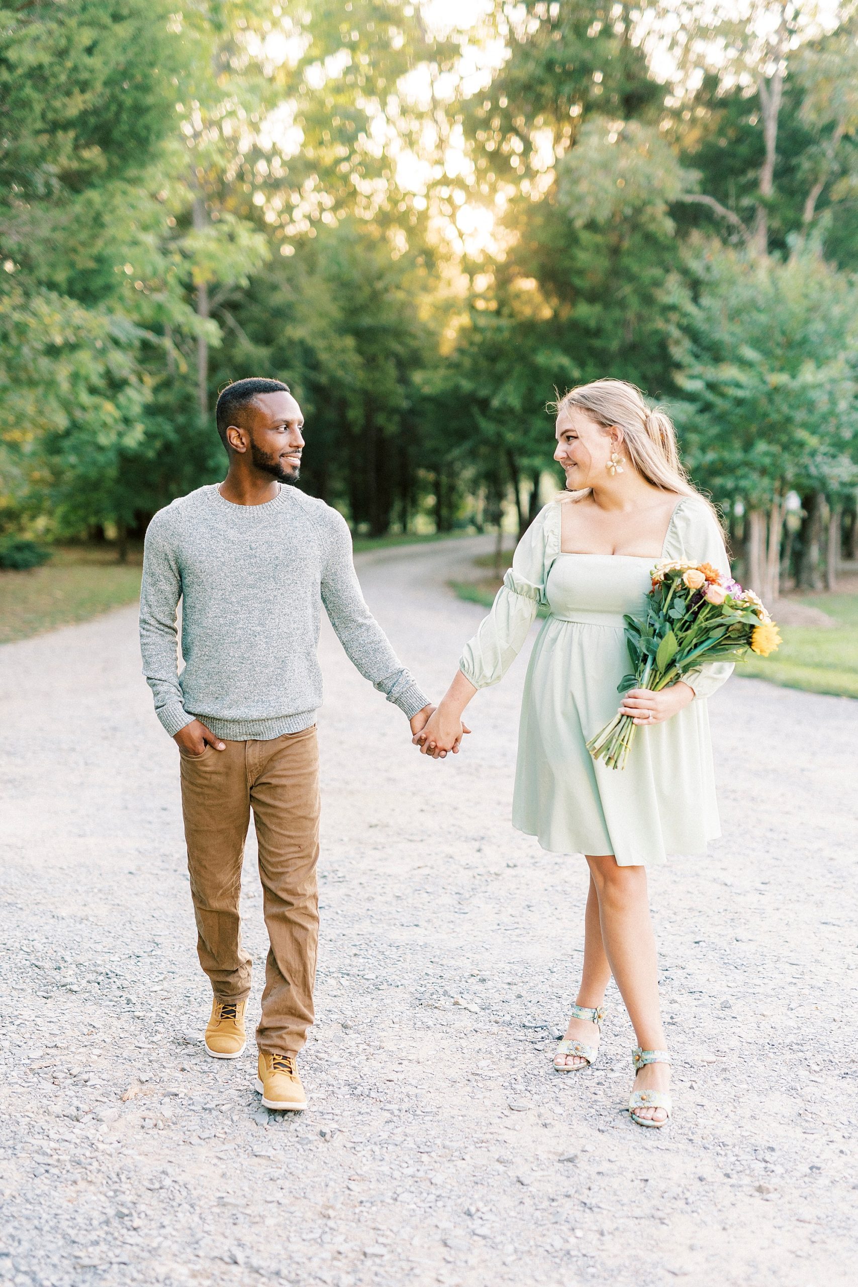 couple holds hands walking on path at Bella Terra while bride holds bouquet