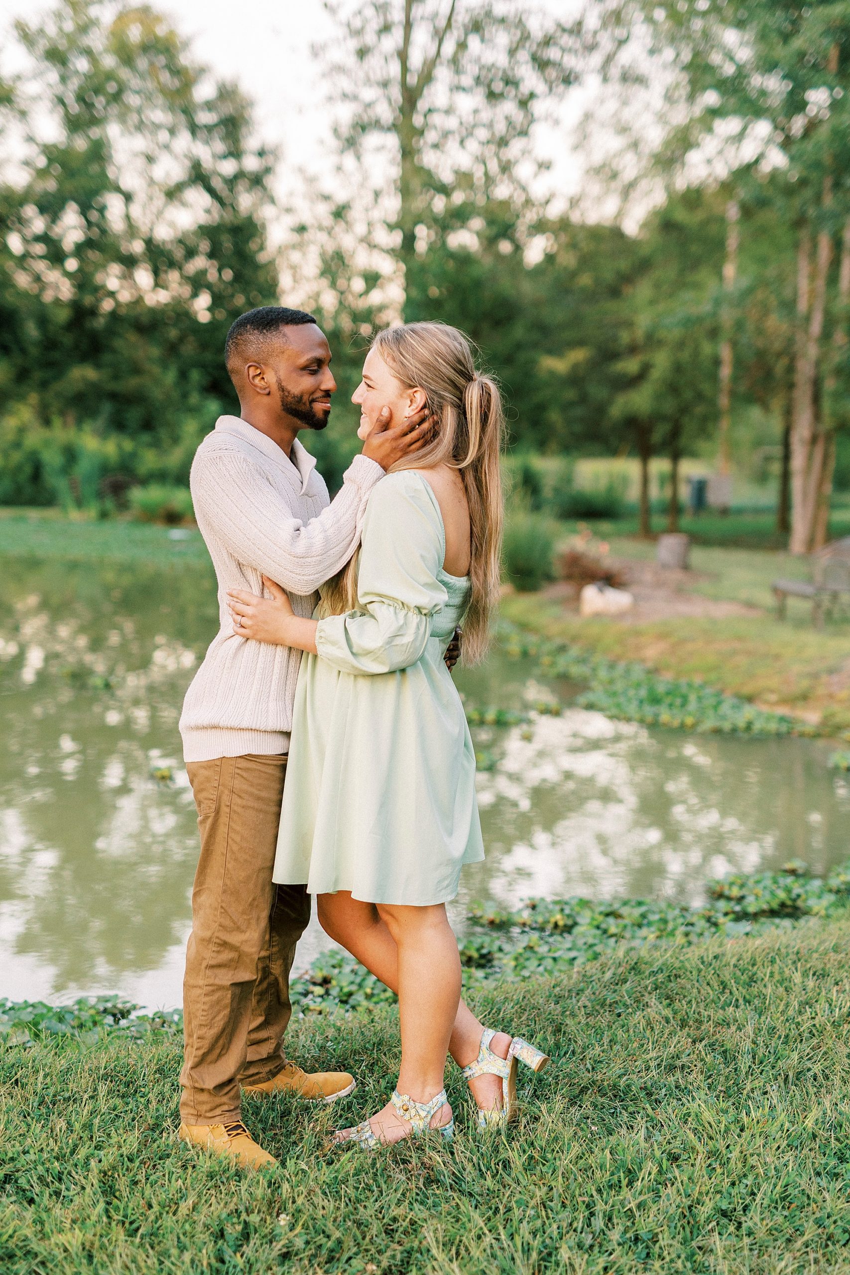 groom holds bride's face leaning in for kiss at pond