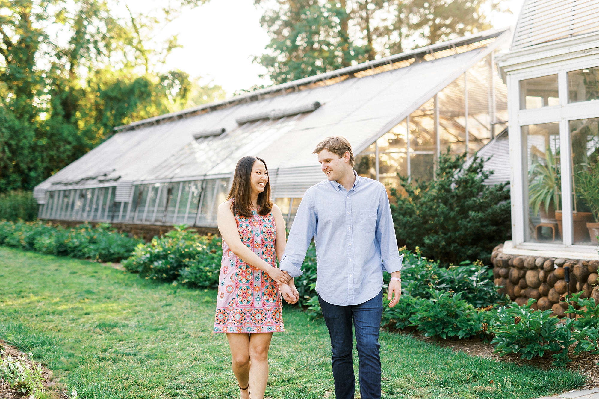 couple holds hands walking on lawn by greenhouse at Reynolda Gardens