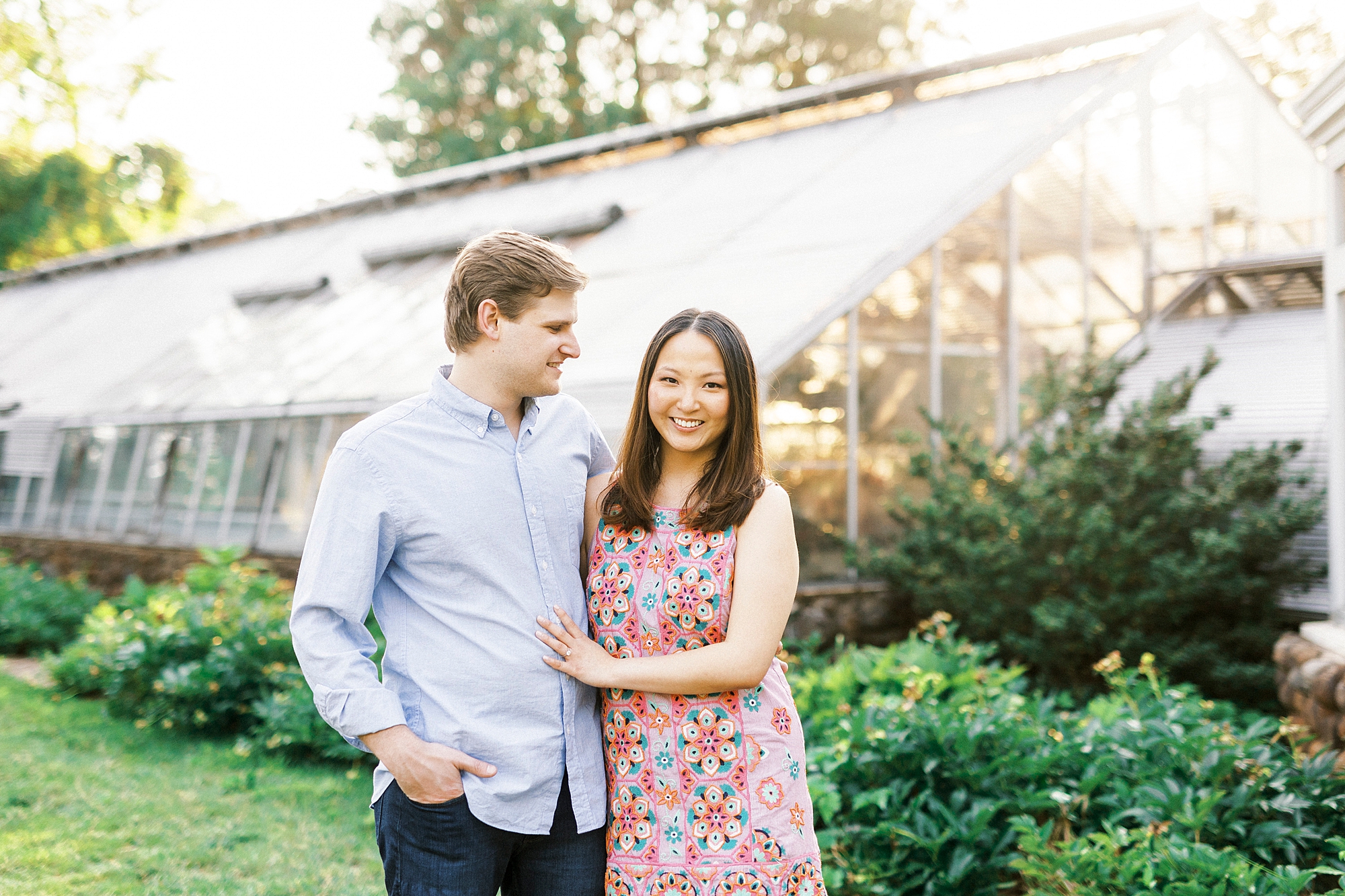 groom in blue shirt looks down at fiancee during Reynolda Gardens engagement portraits