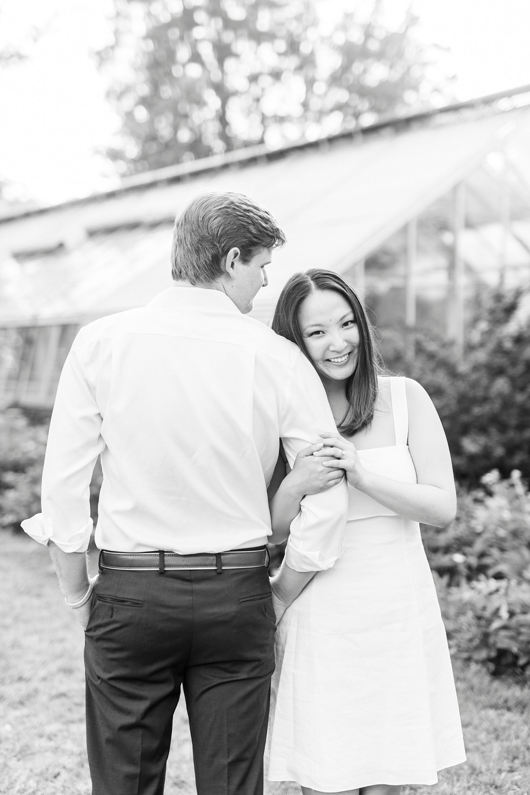 woman leans on fiancee's arm standing by greenhouse at Reynolda Gardens