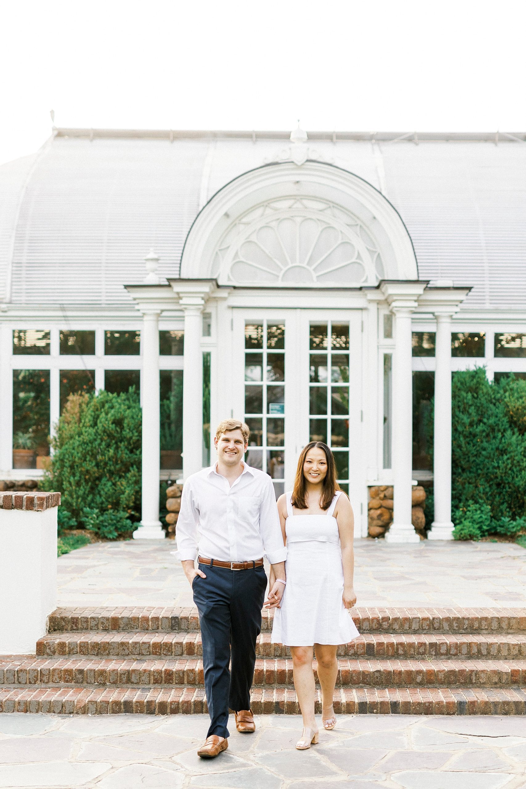 couple holds hands walking by conservatory at Reynolda Gardens