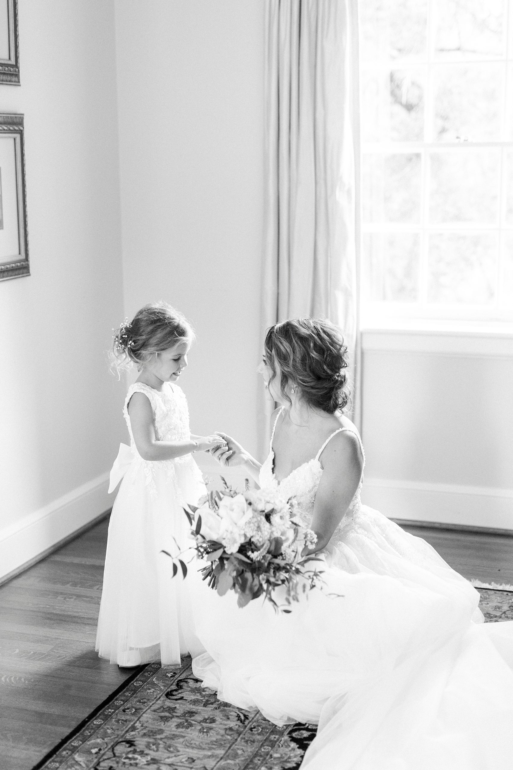 bride kneels down to talk to flower girl in bridal suite