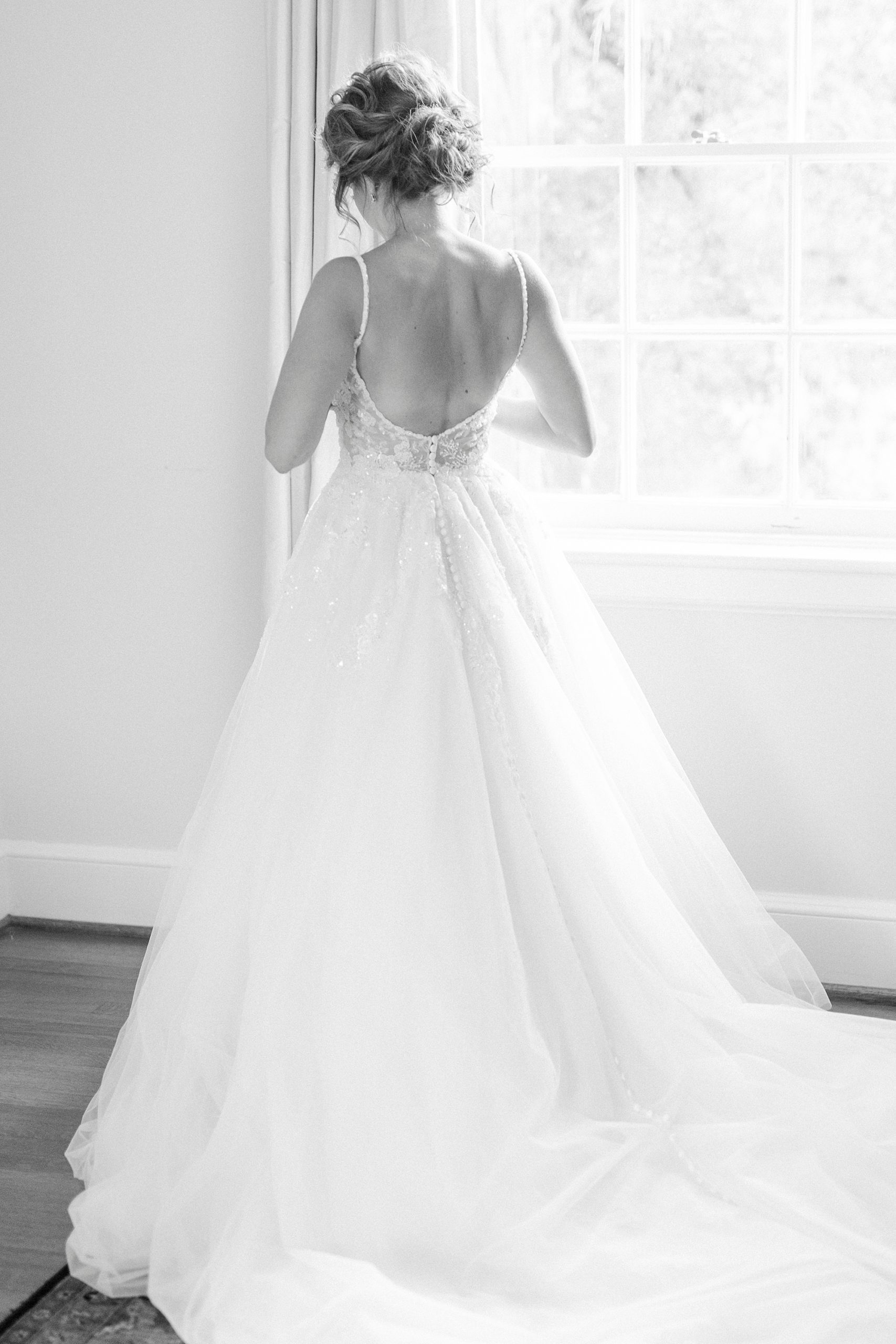 bride looks out window at Boxwood Estate showing off back of gown