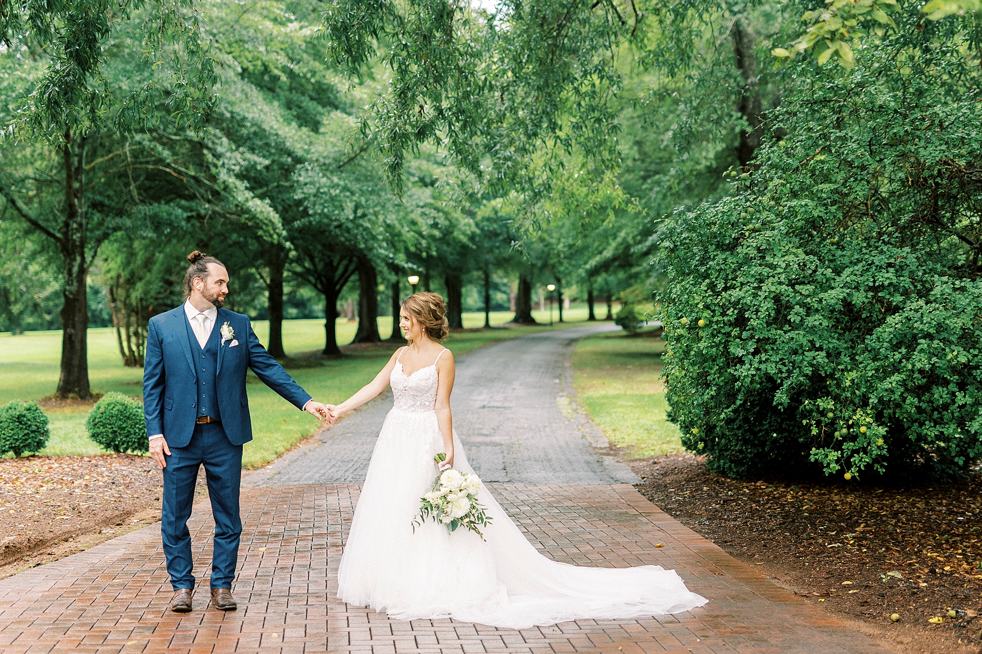 couple holds hands on brick walkway at Boxwood Estate