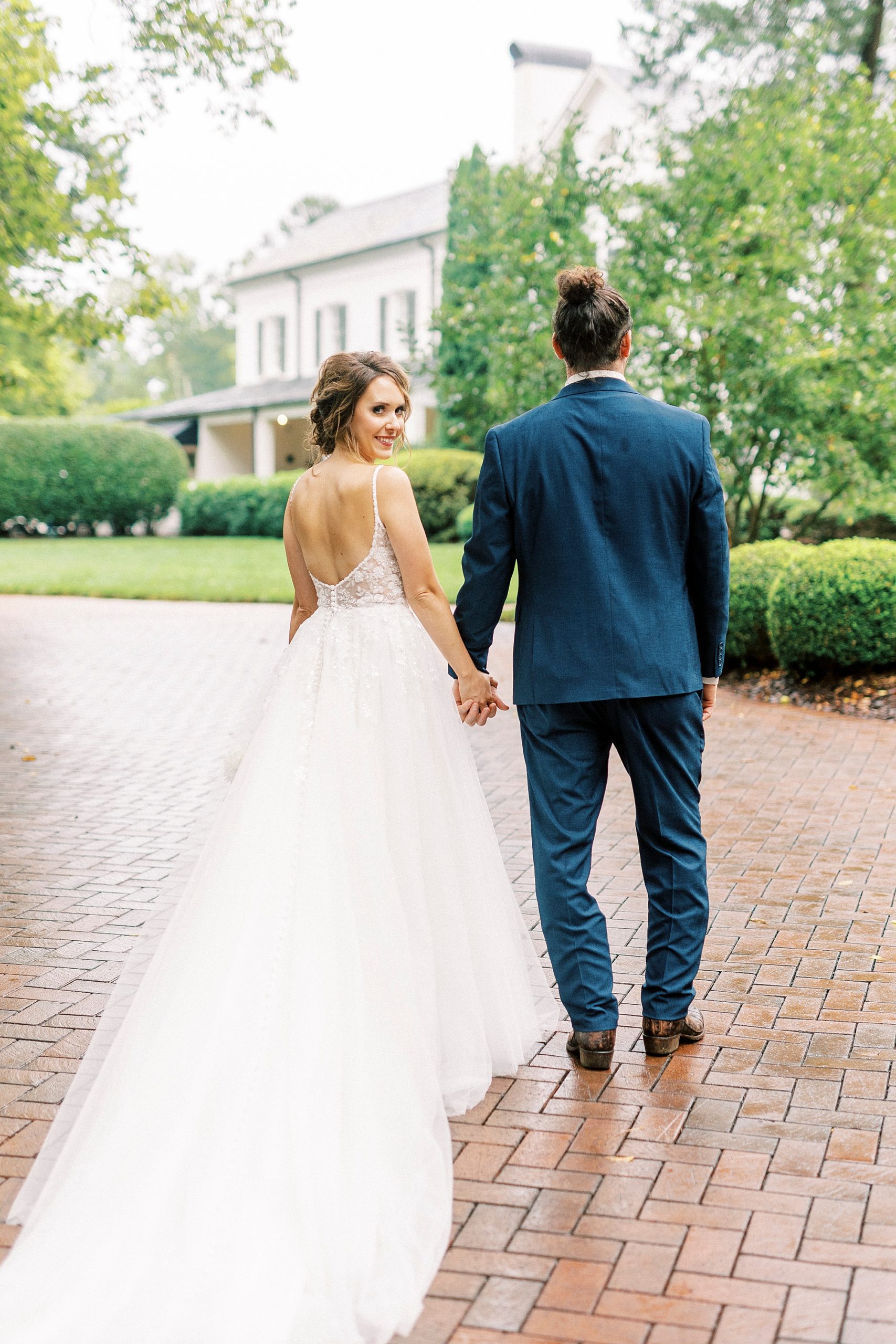 bride and groom walk on pathway while bride looks over shoulder