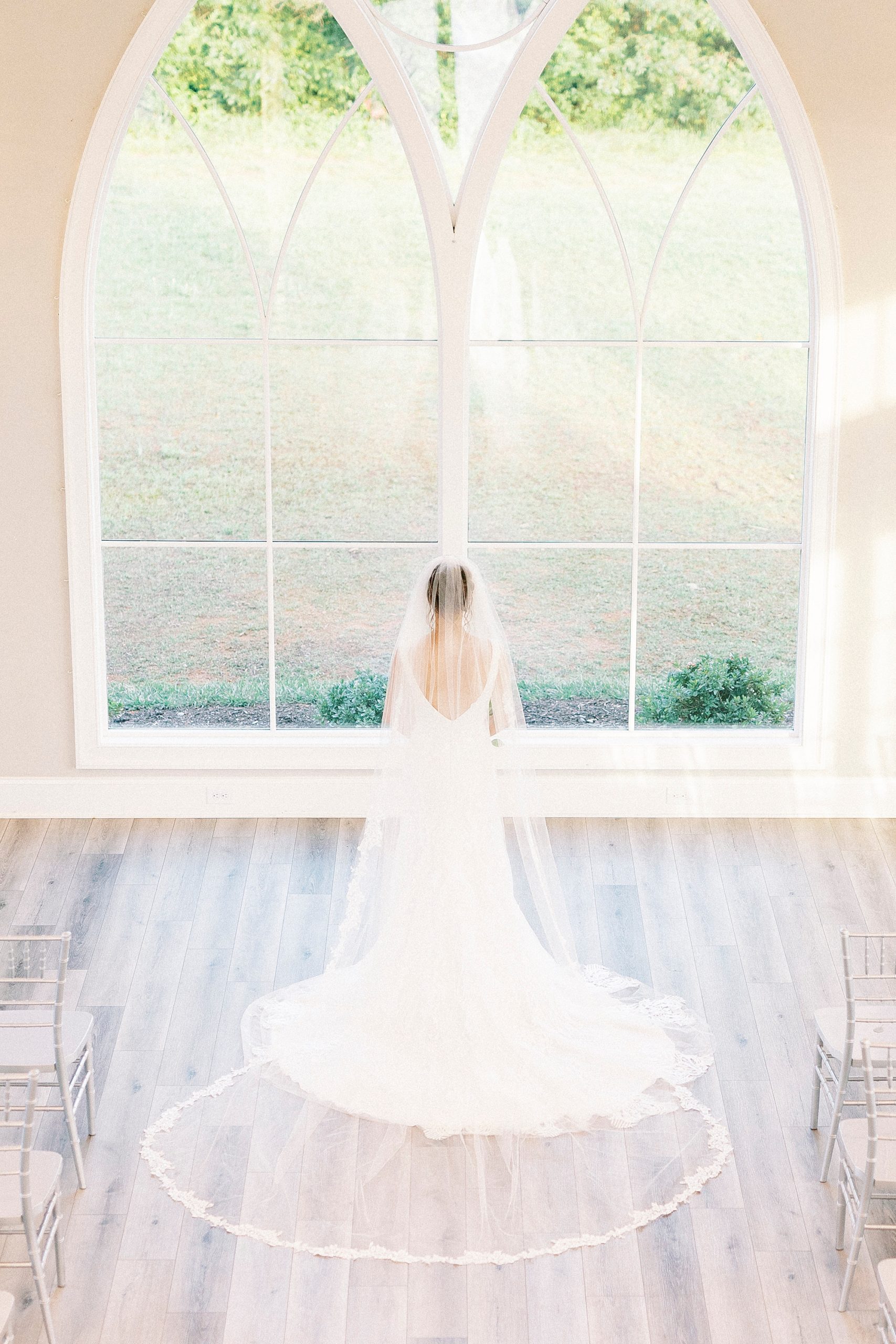 bride looks out windows at Chickadee Hill Farms with veil behind her 