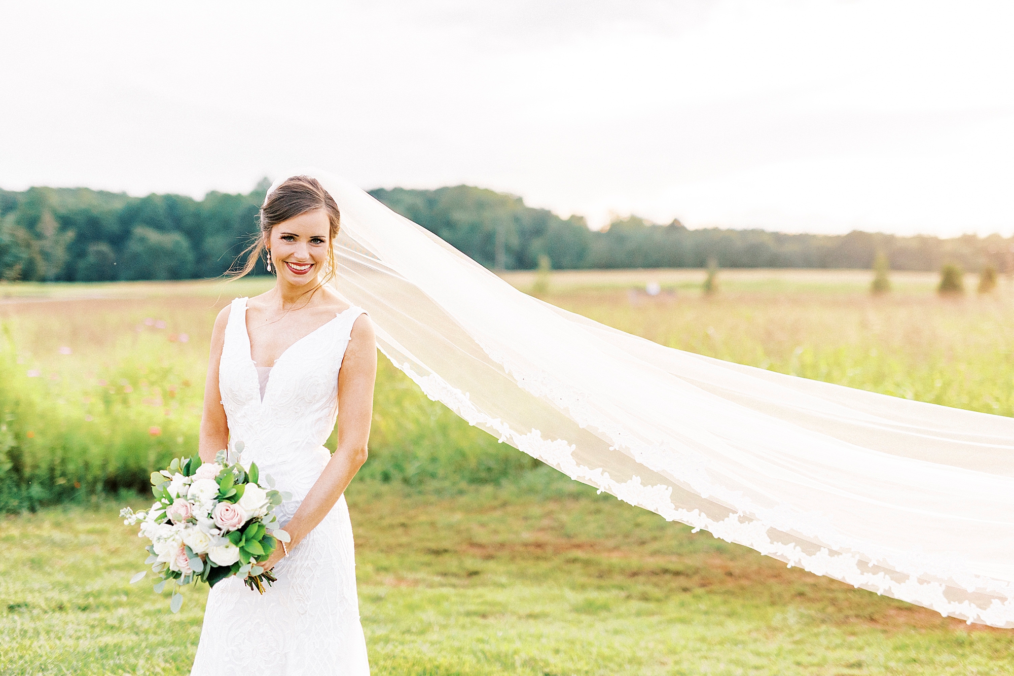 bride holds bouquet by stomach with veil floating behind her