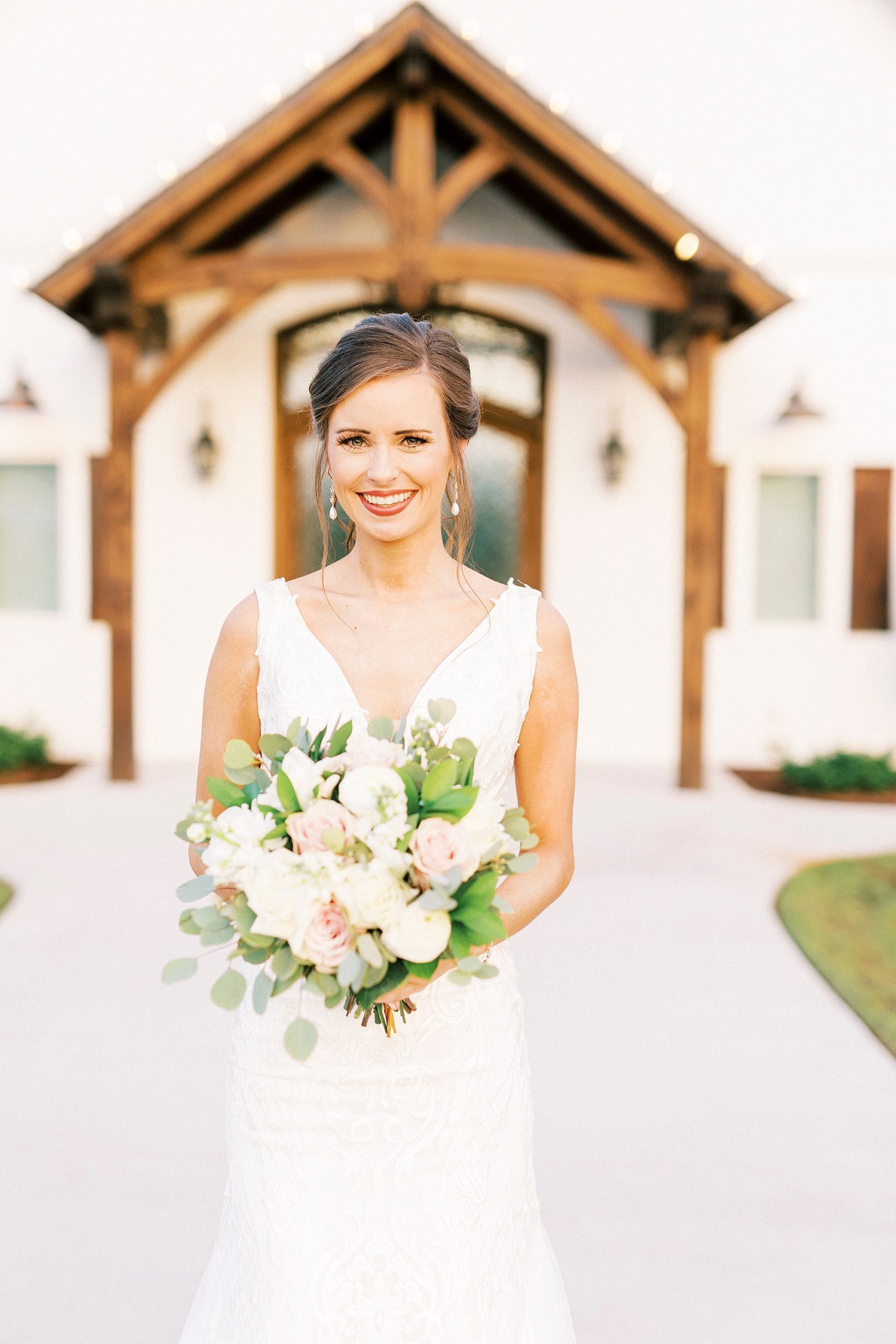 bride stands holding bouquet of white and pink flowers outside wooden arch at Chickadee Hill Farms