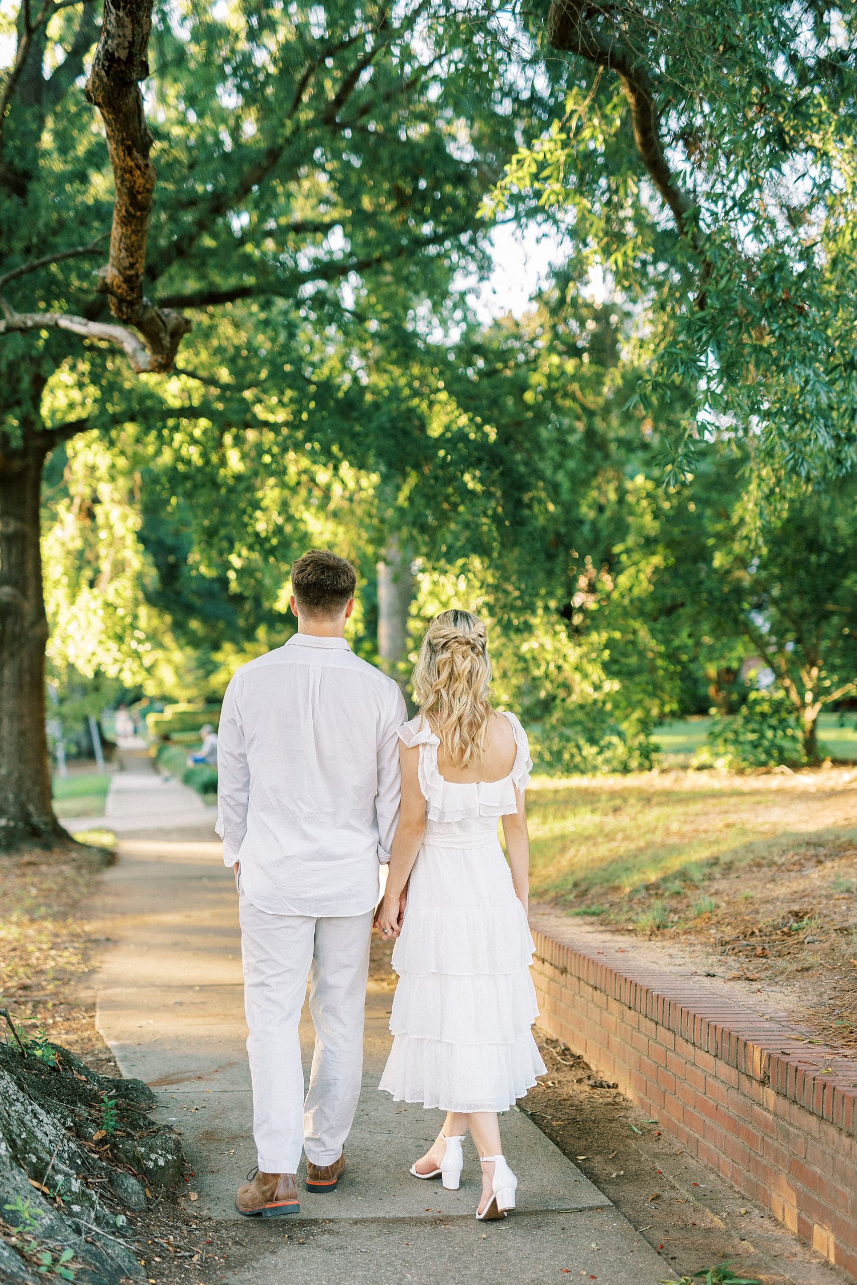 engaged couple holds hands walking down sidewalk during Downtown Concord engagement portraits
